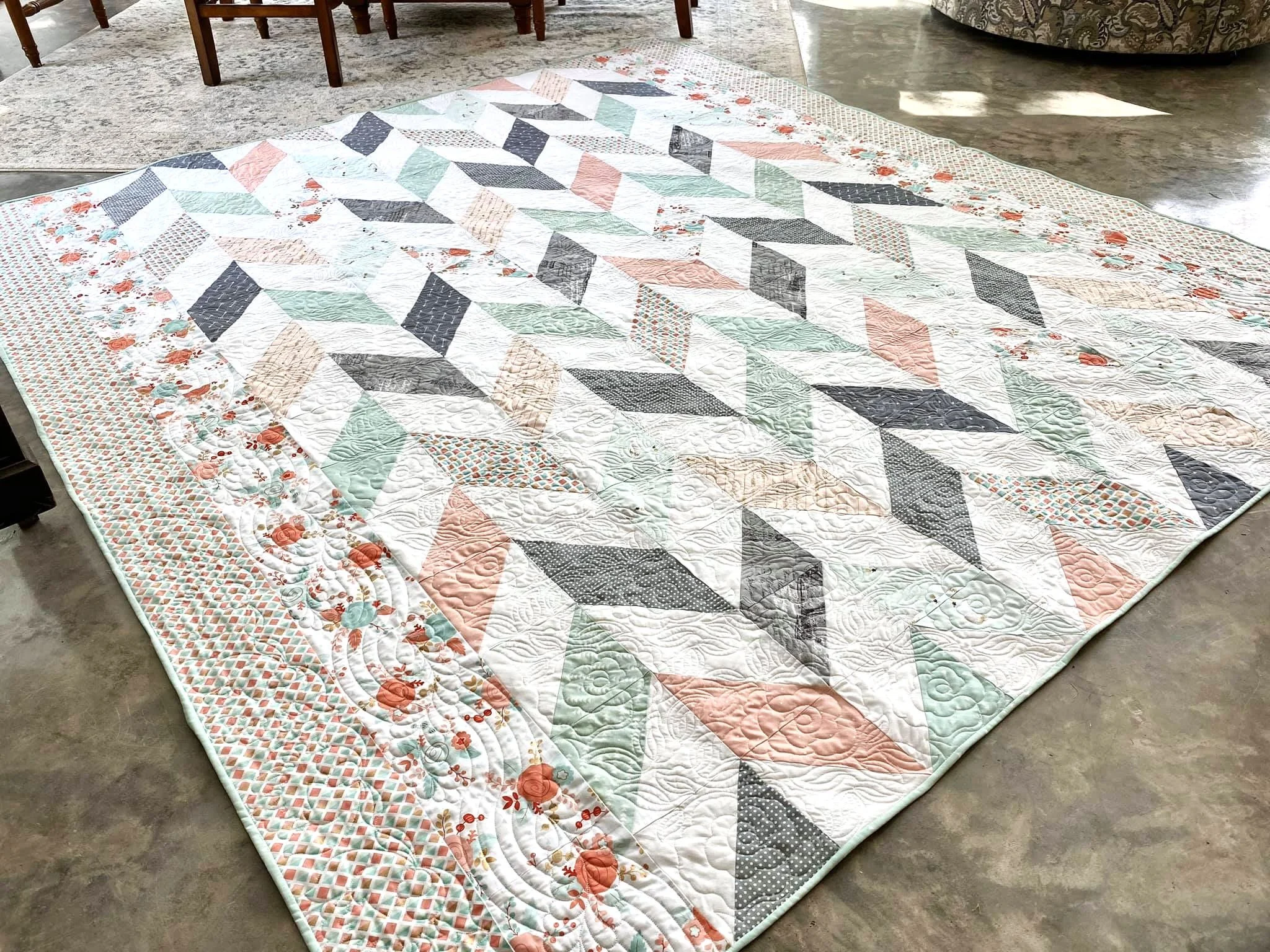 Colorful quilt with geometric and floral patterns on a floor, with furniture around.