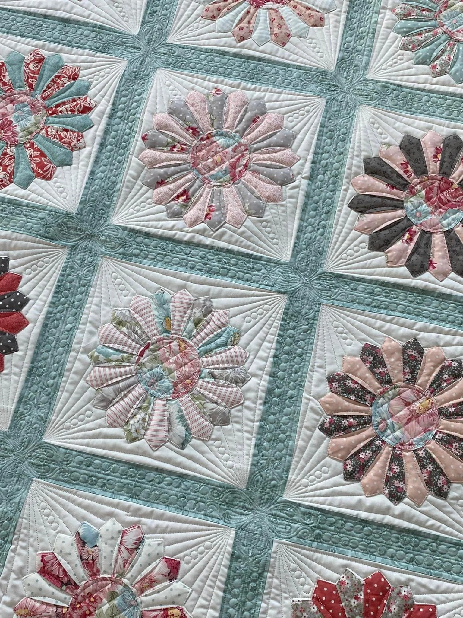 Close-up of a quilt with floral patterns in pastel colors, featuring interconnected square blocks with applique flower designs surrounded by decorative quilting.