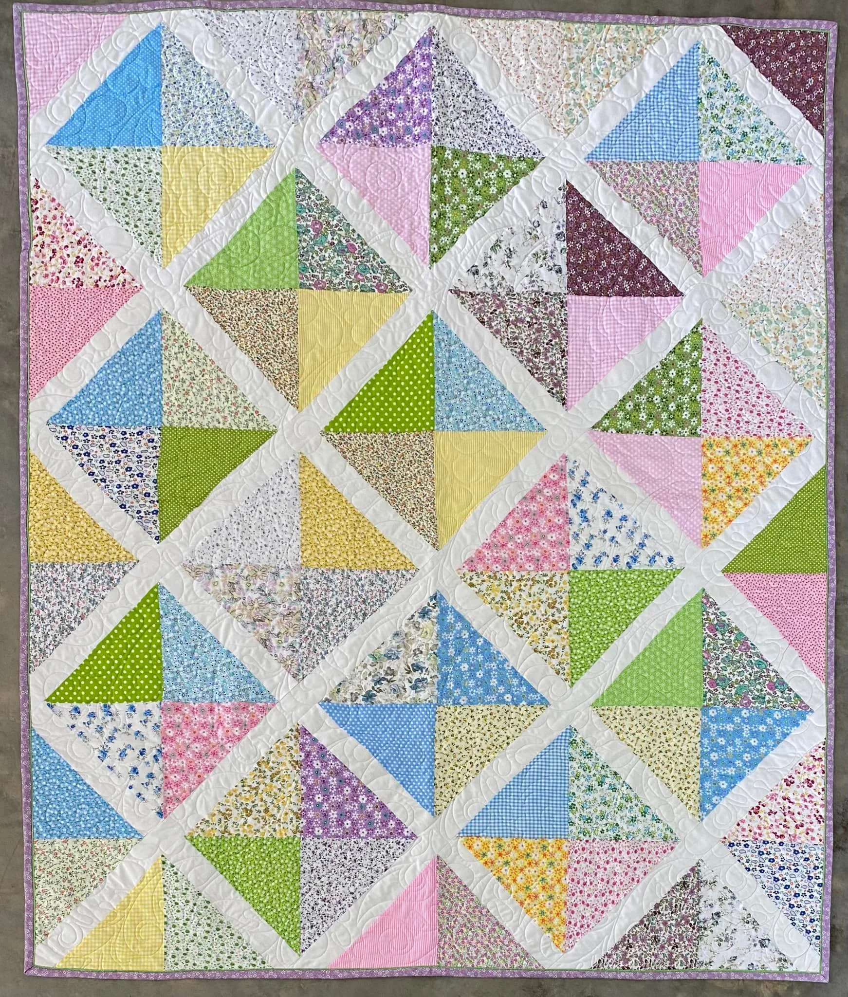 Colorful quilt with pink, green, yellow, blue, and purple floral and gingham patterns, arranged in a diamond block pattern, with white sashing and purple border.