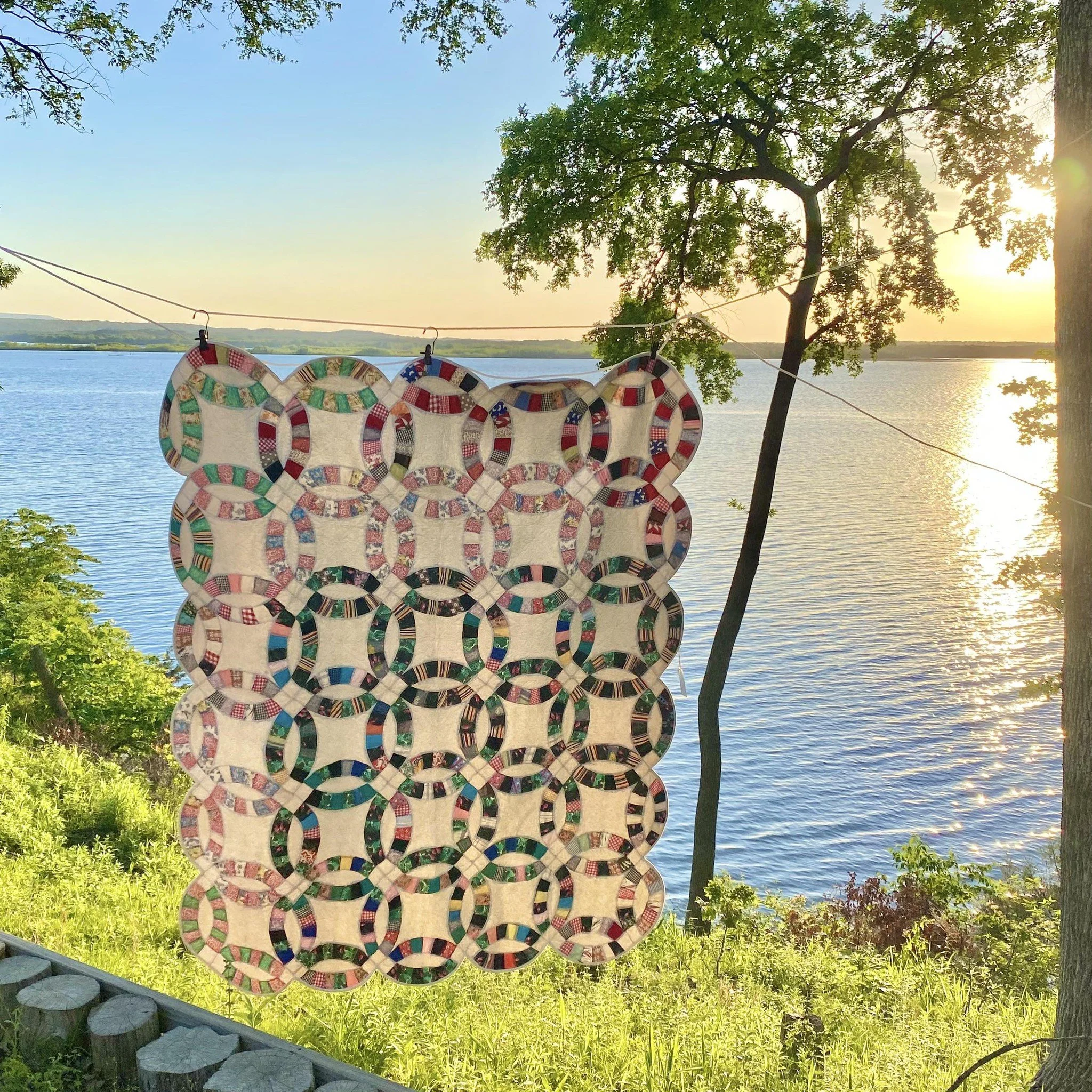 Colorful quilt hanging on a line near a lake at sunset.