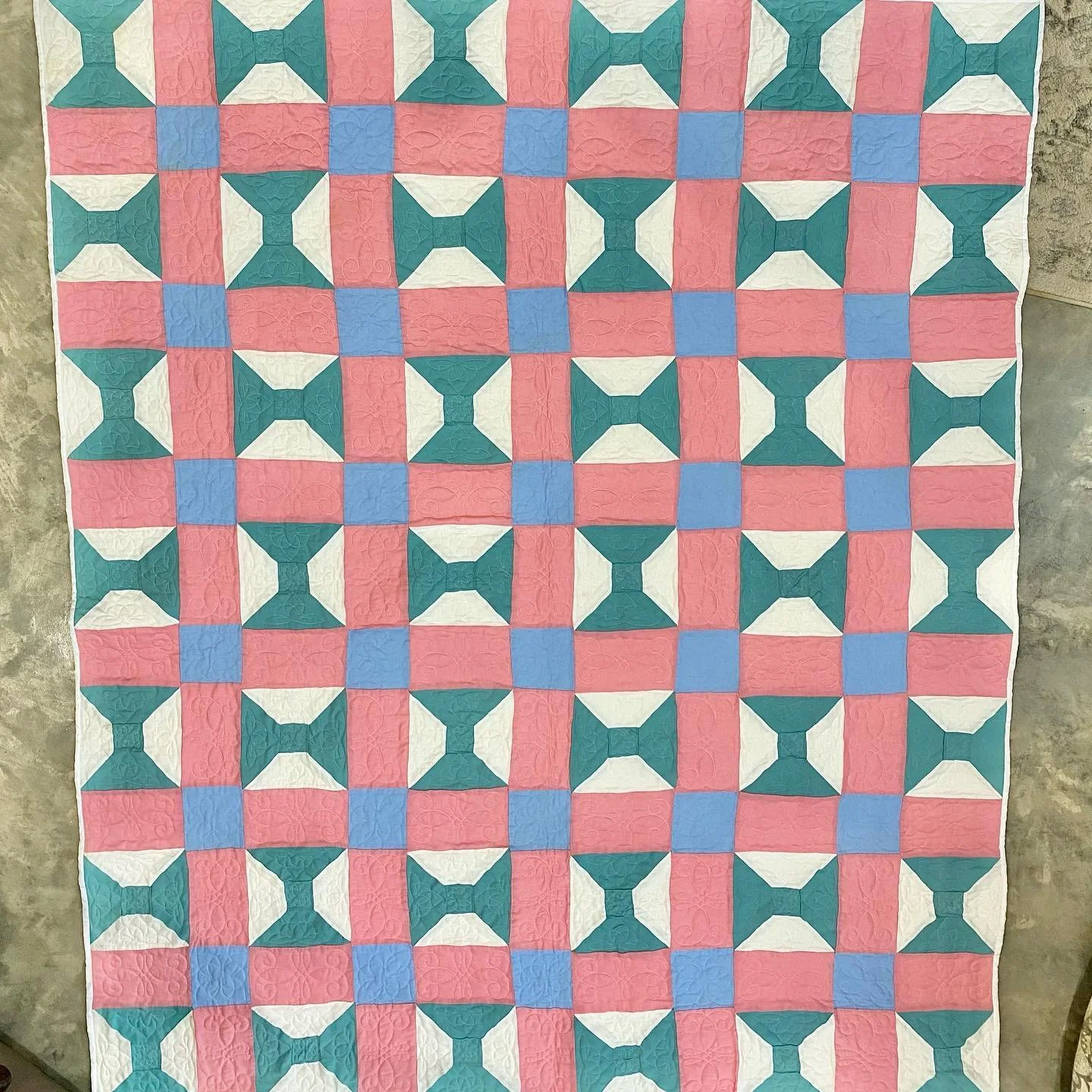 A colorful quilt with a geometric pattern of pink, white, blue, and green shapes arranged in a repeating design.