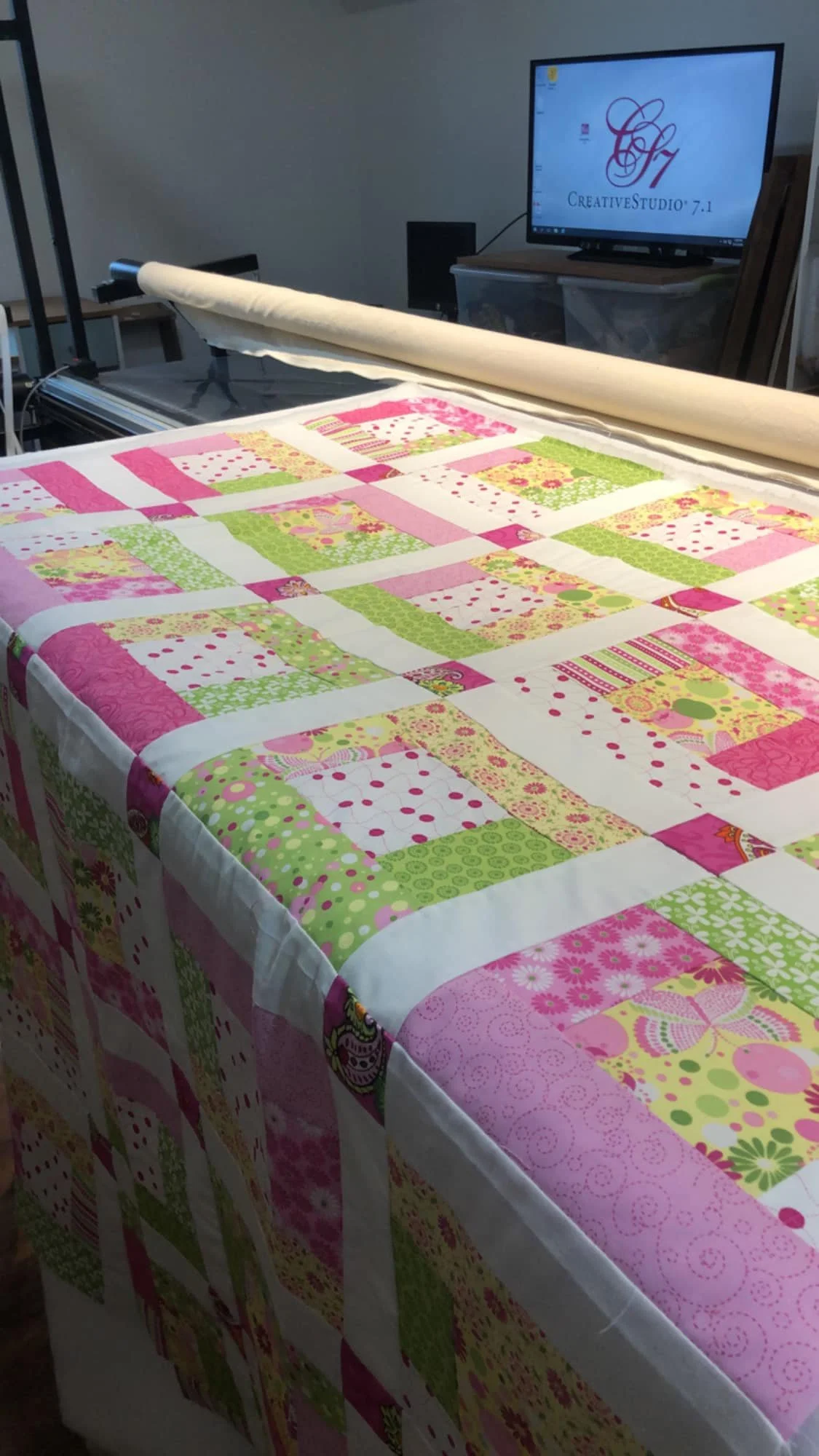 A colorful patchwork quilt with pink, green, yellow, and white patterns on a quilting machine.