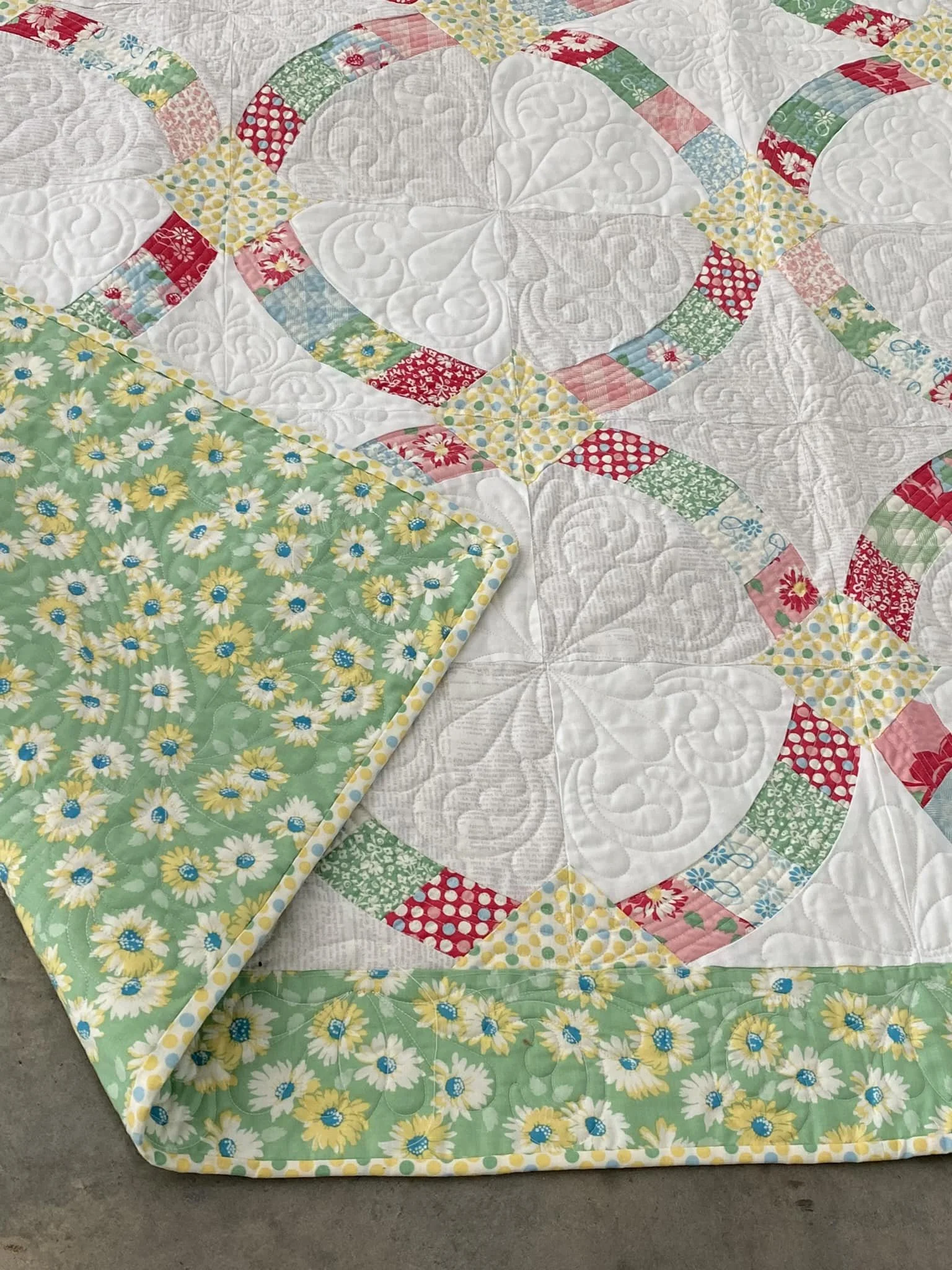 A quilt with a white background and a border decorated with yellow and white daisies on a green background.
