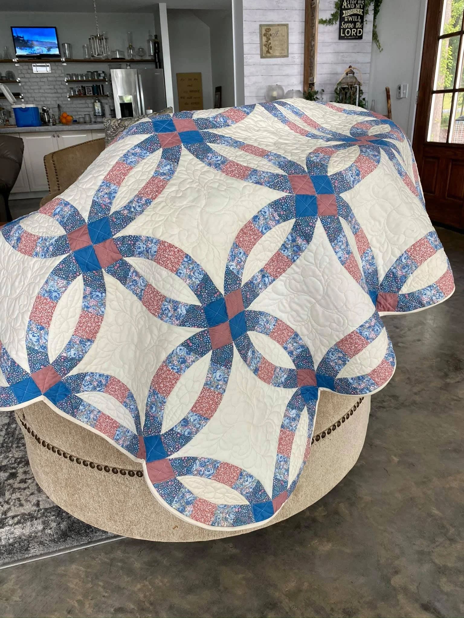 A quilt with alternating blue and red floral patterns arranged in a geometric circle design, draped over a beige cushioned chair in a cozy home setting.