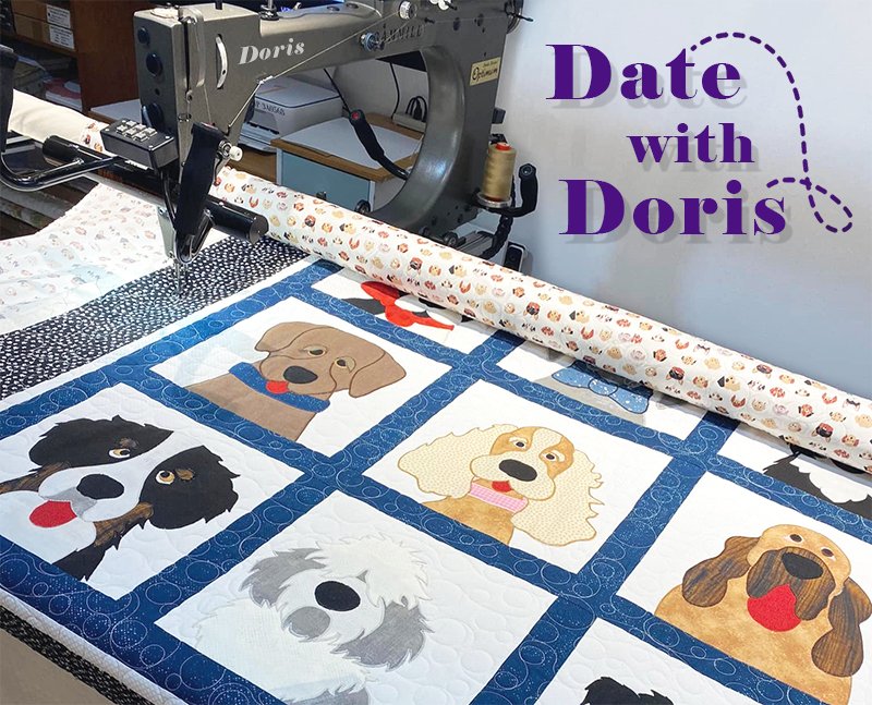 A longarm sewing machine is quilting a colorful dog-themed quilt. Each square features a different dog breed. The quilt has a blue border with circular patterns.