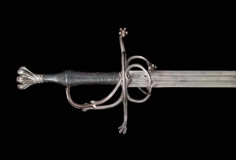A close-up of a medieval sword with a decorated hilt and a plain metal blade against a black background.