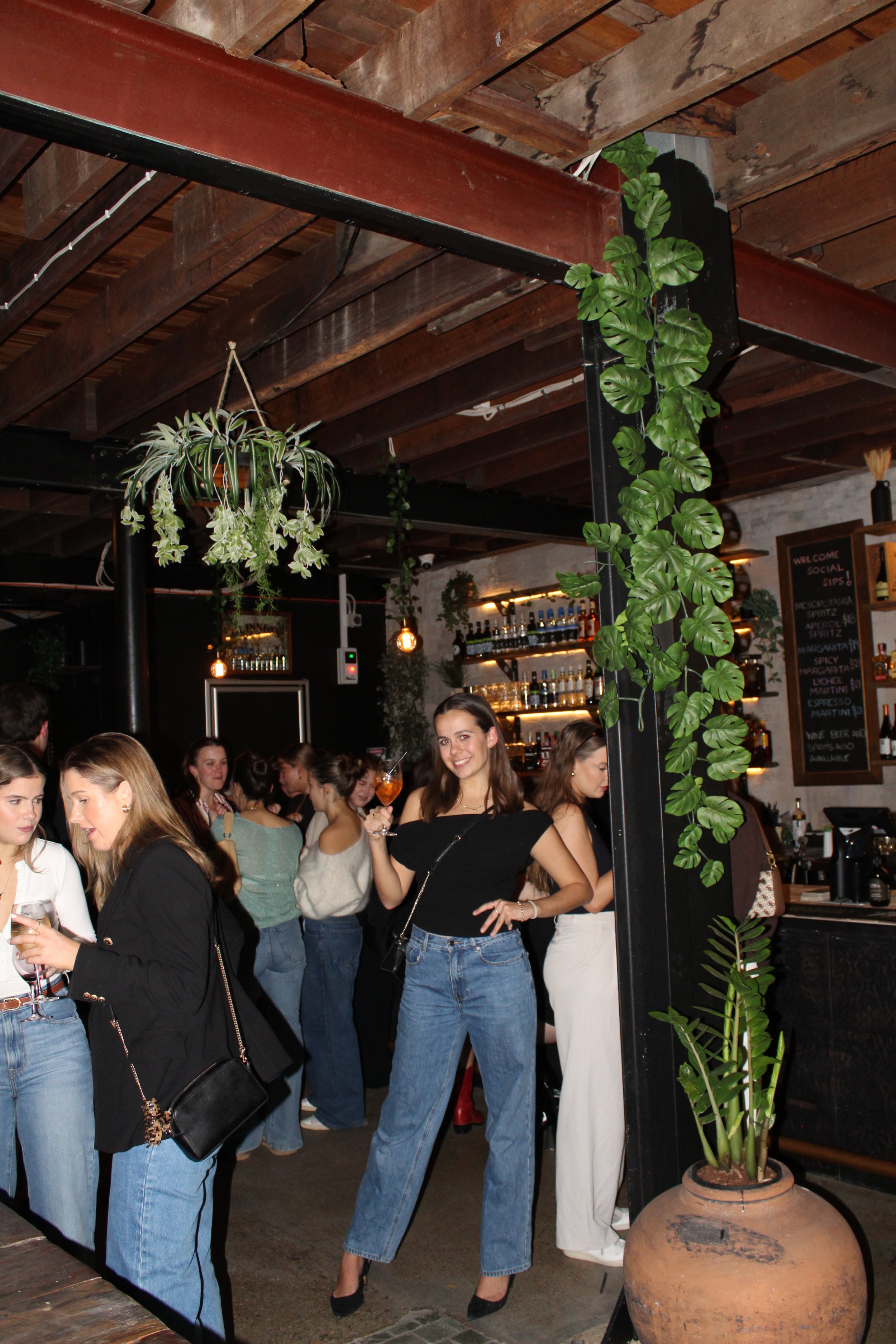 Group of women at a bar during a social night, with one woman holding a drink and smiling at the camera.