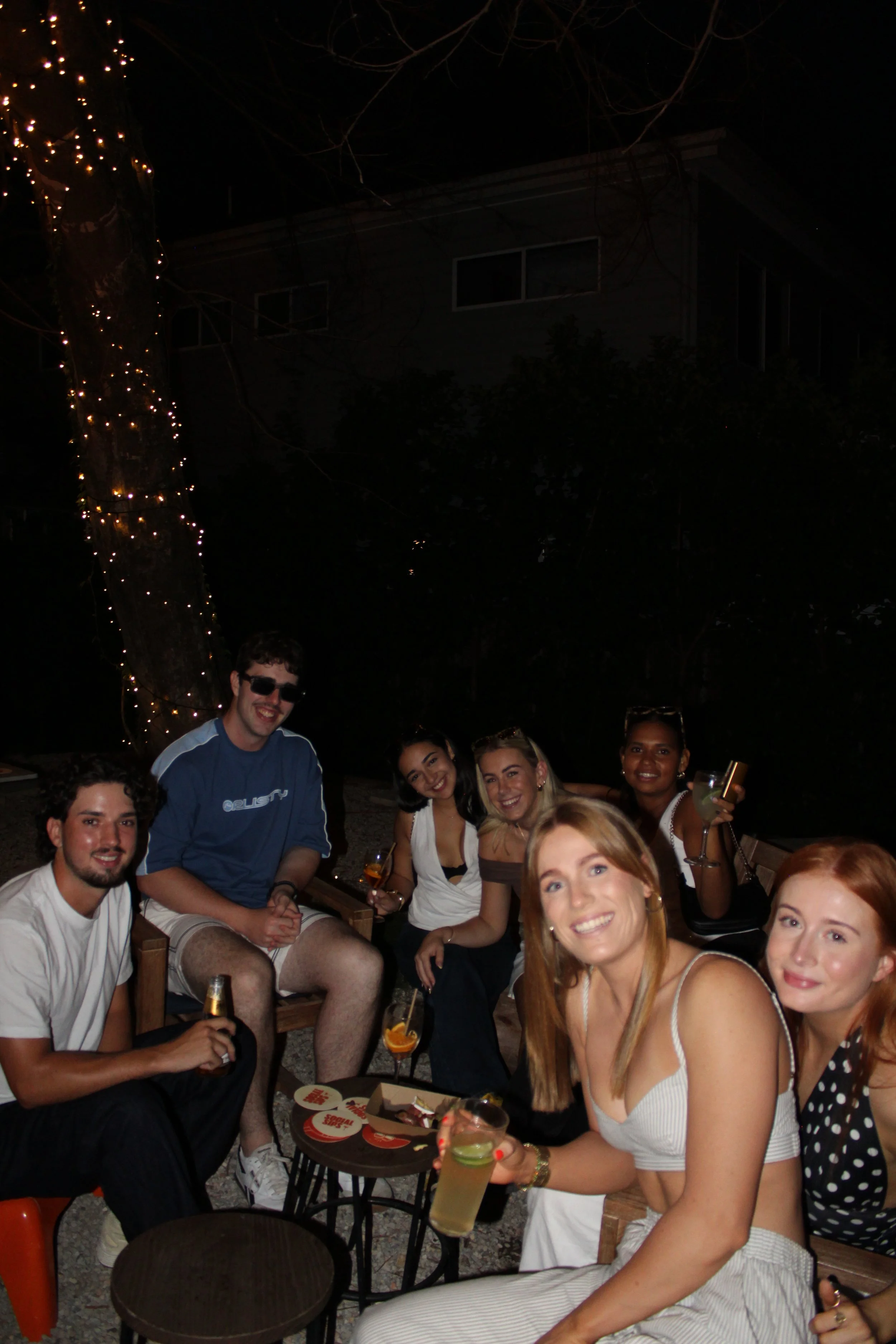 Four women smiling and posing together at a bar, one holding a glass of wine.