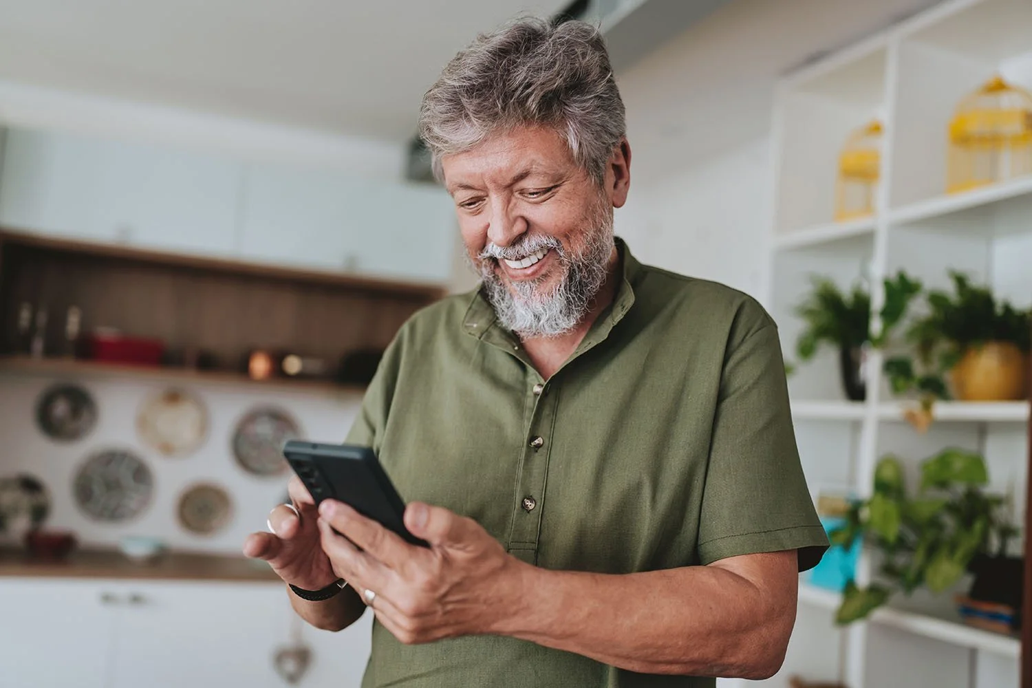 Older Latino man smiling while using his phone for an online therapy session, accessing telehealth mental health services with a culturally responsive therapist in California.