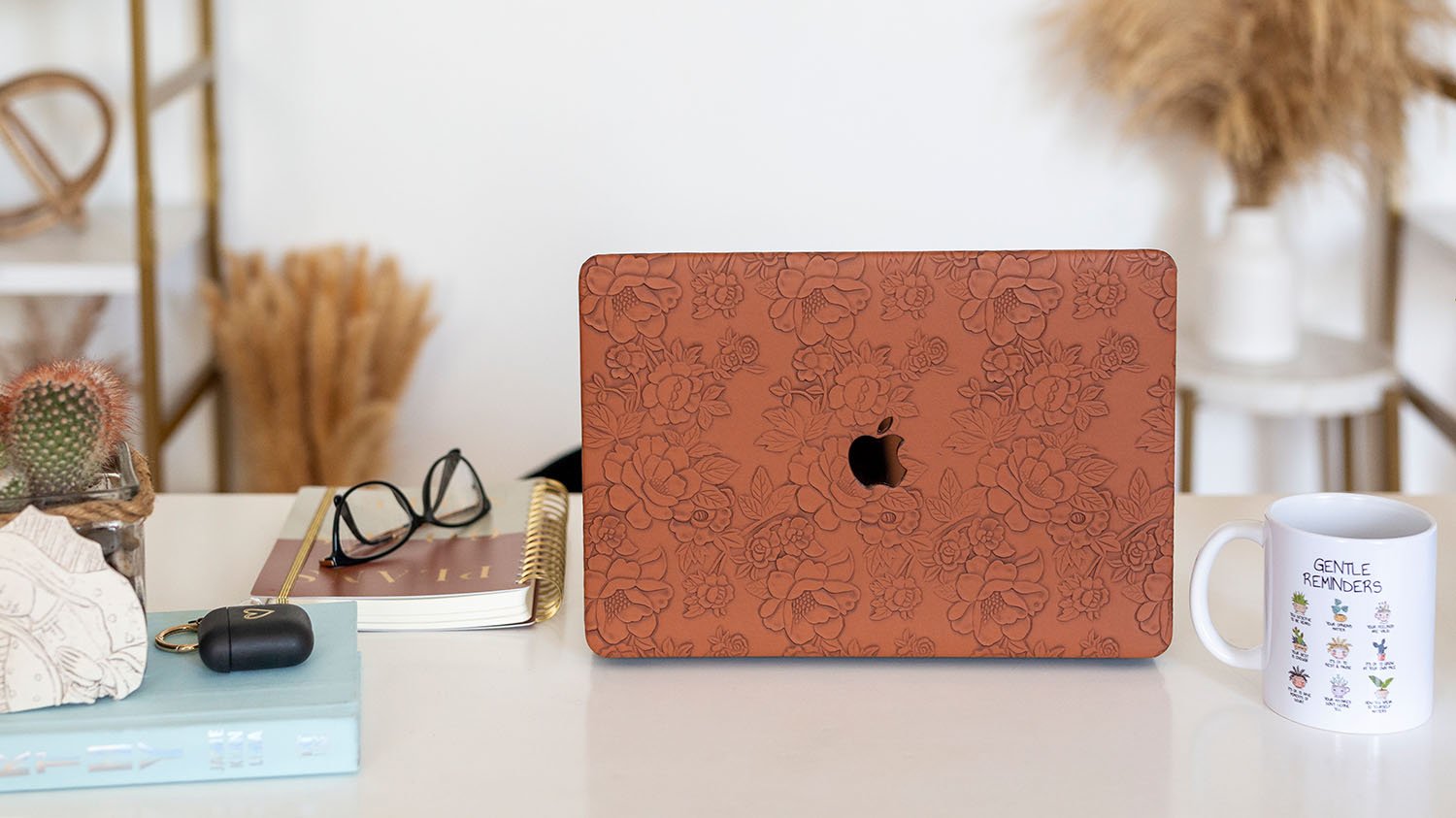 A laptop with a floral cover sits on a calm, light-filled desk next to a mug, representing a welcoming and supportive online therapy space.