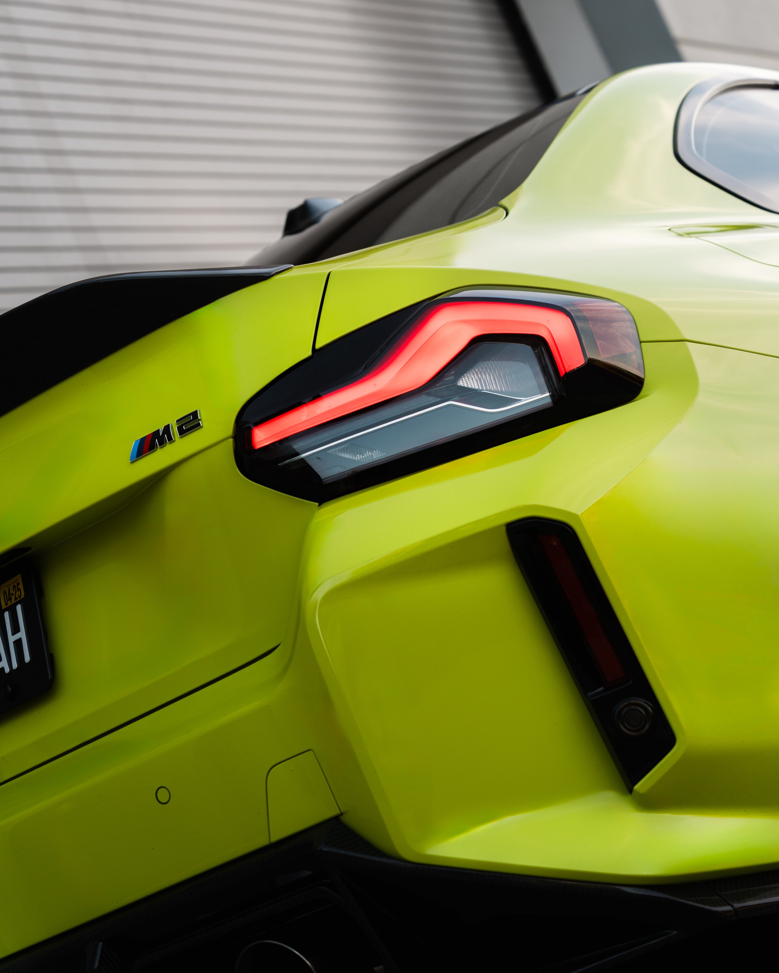 Rear view of a bright yellow BMW M2 sports car showing its taillight and trunk.