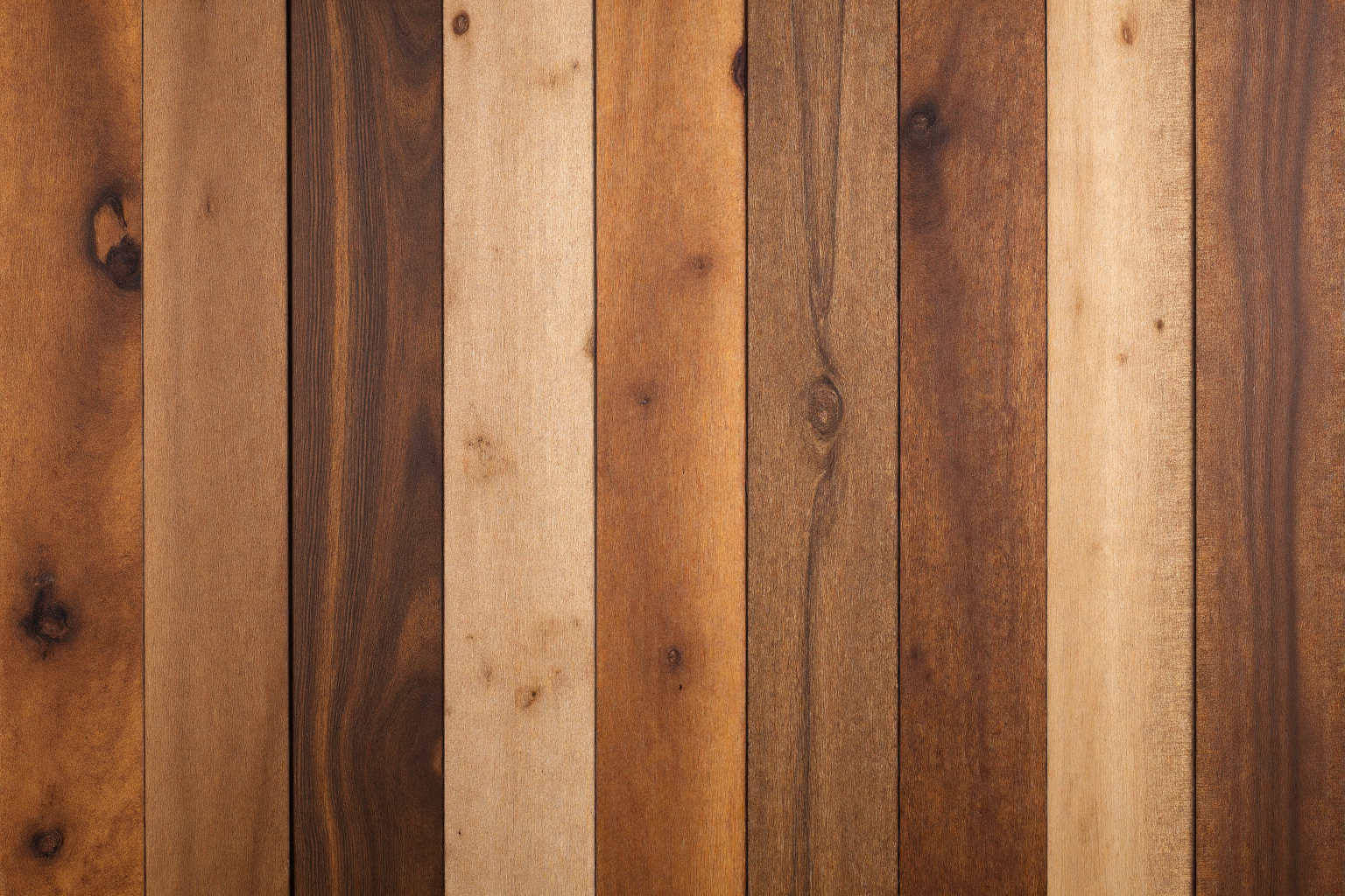 A sanded and refinished hardwood floor made of vertically aligned oak pine birch wood planks stained with different natural grain and warm brown tones.