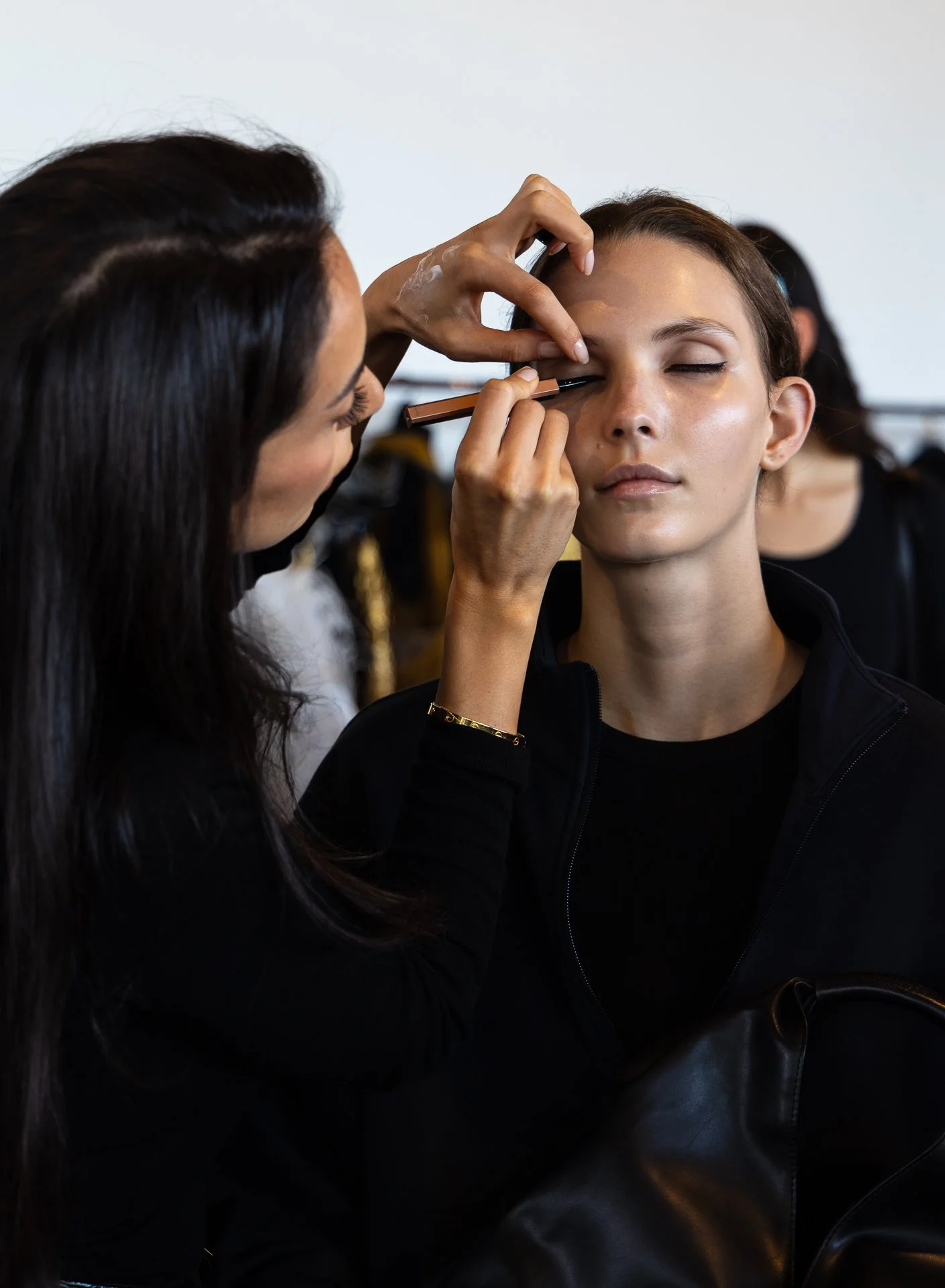 Makeup artist applying eye makeup to a woman's face in a studio.