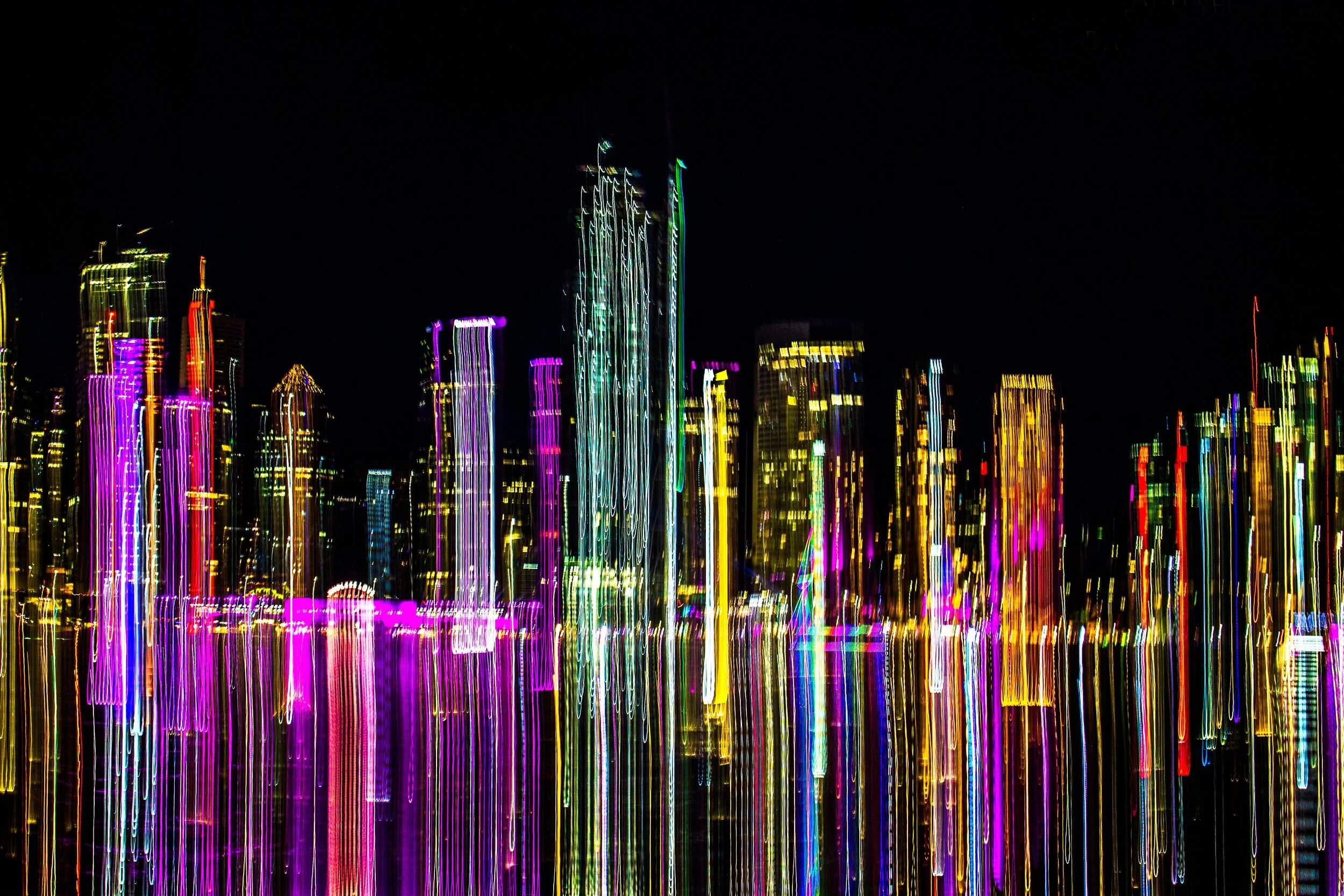 Colorful illuminated city skyline at night with tall buildings and bright neon lights, slightly blurred.