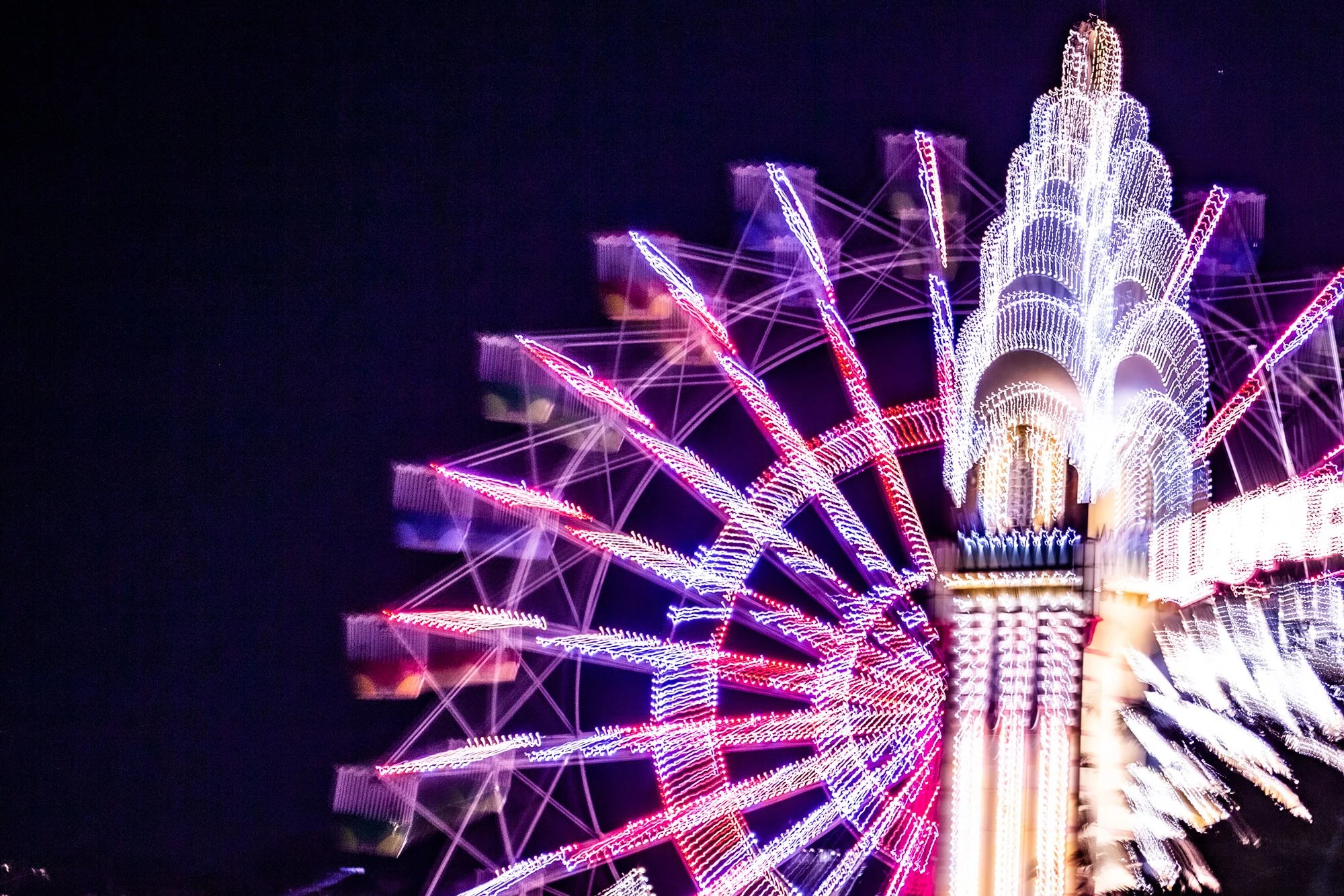 Brightly lit amusement park ride at night with colorful neon lights creating a circular pattern.