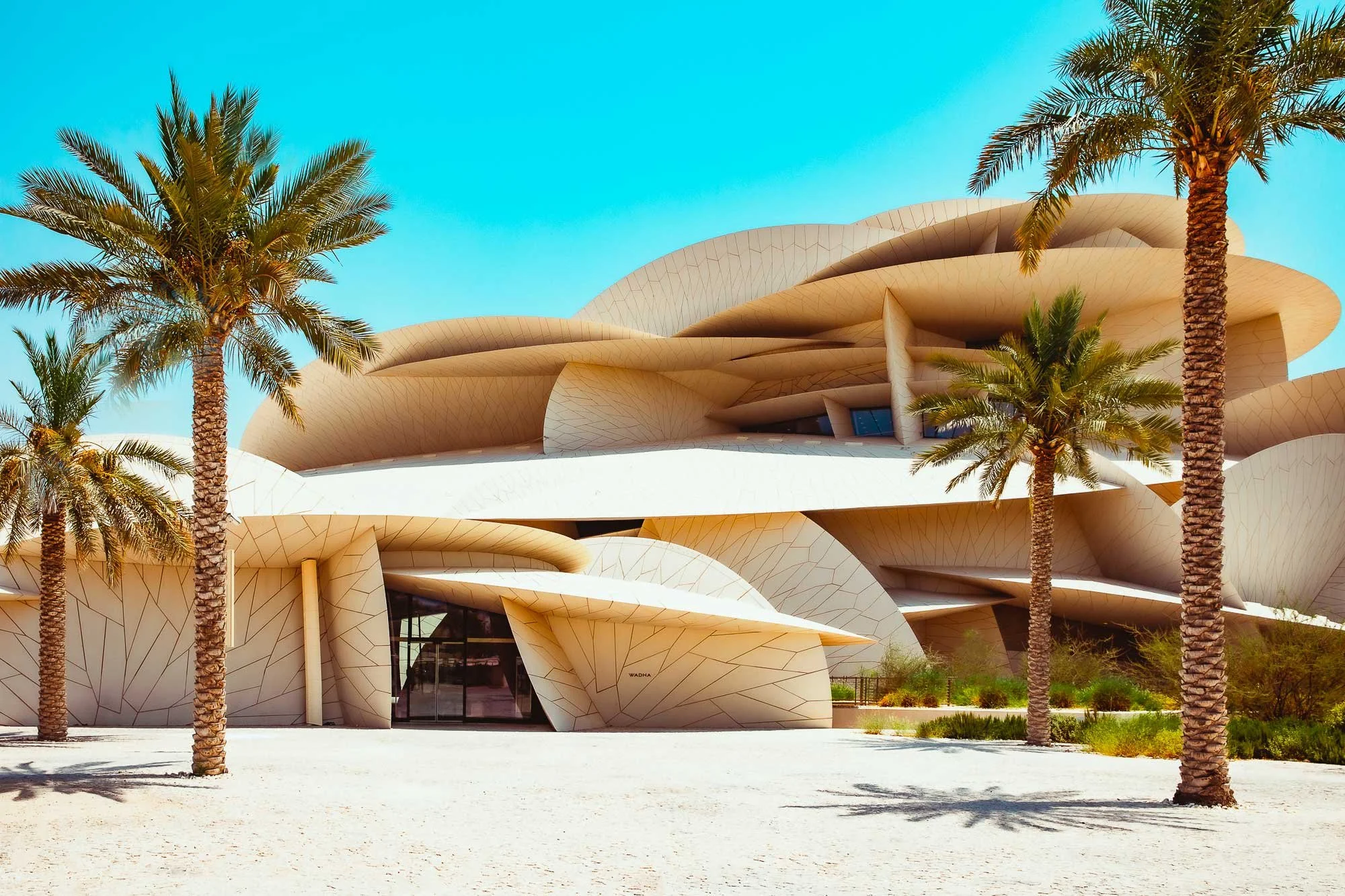 Modern architectural building with curved, layered design and palm trees in front.