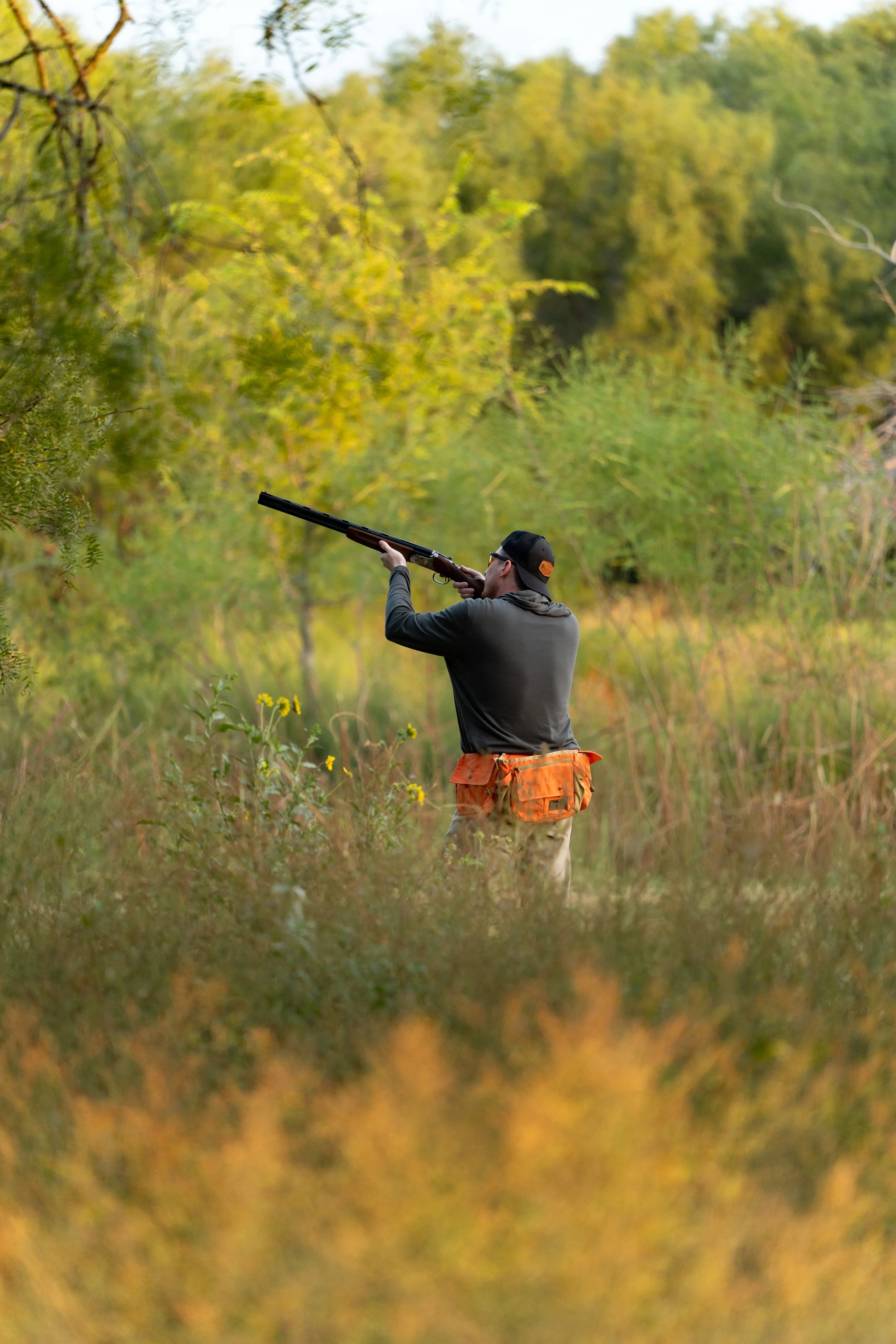 A person hunting with a shotgun in a wooded area during daytime.