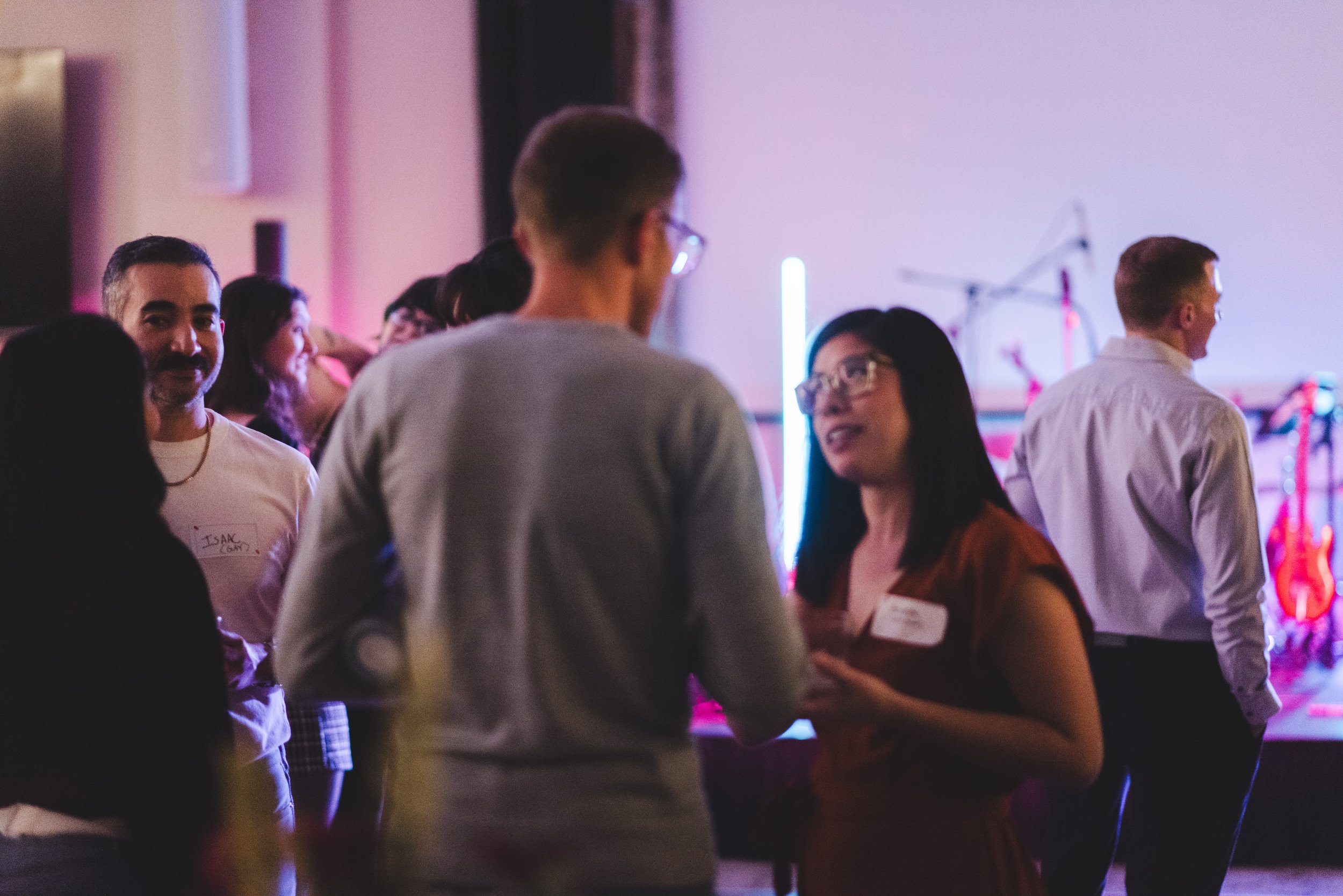 Group of people talking and socializing at a party or event with colorful lights and a dark background.
