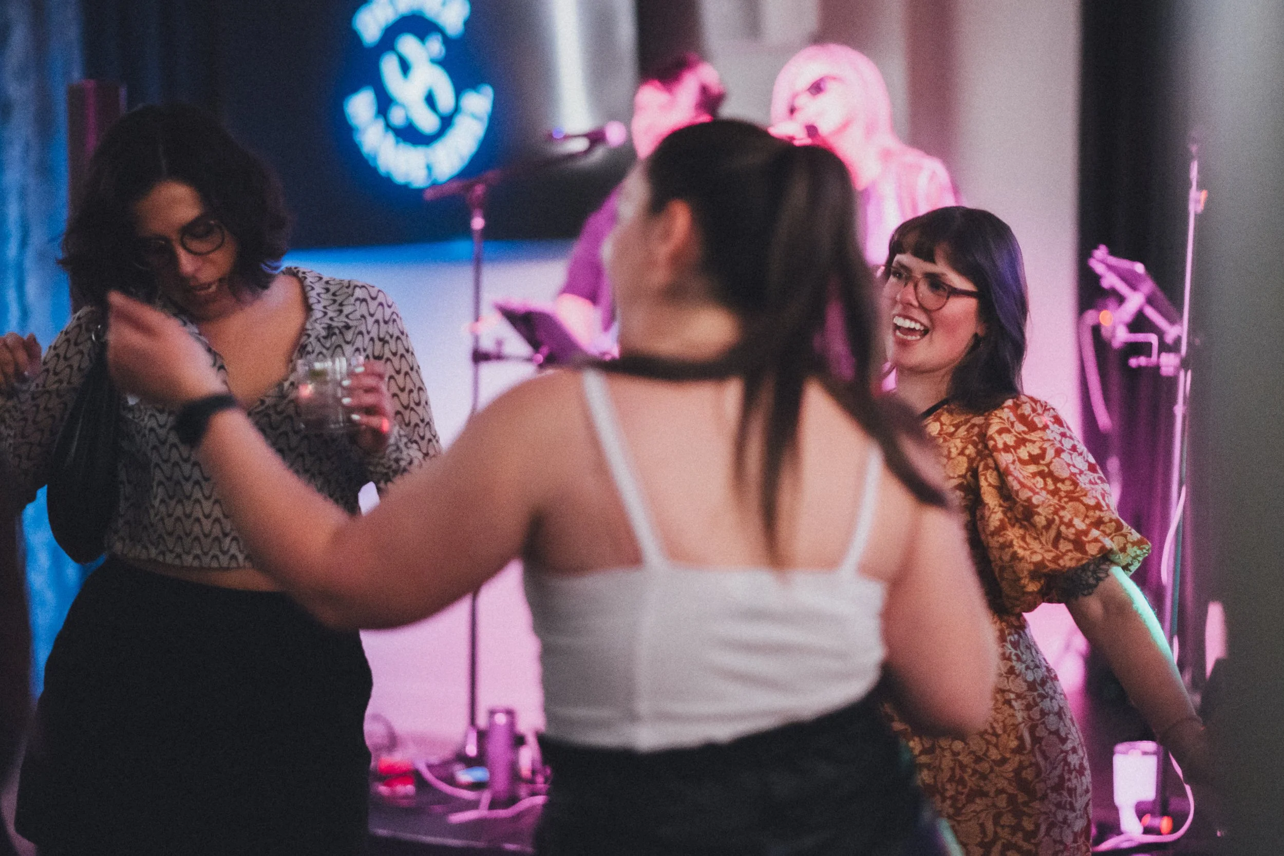 Group of women dancing and socializing at a party with colorful neon lighting.