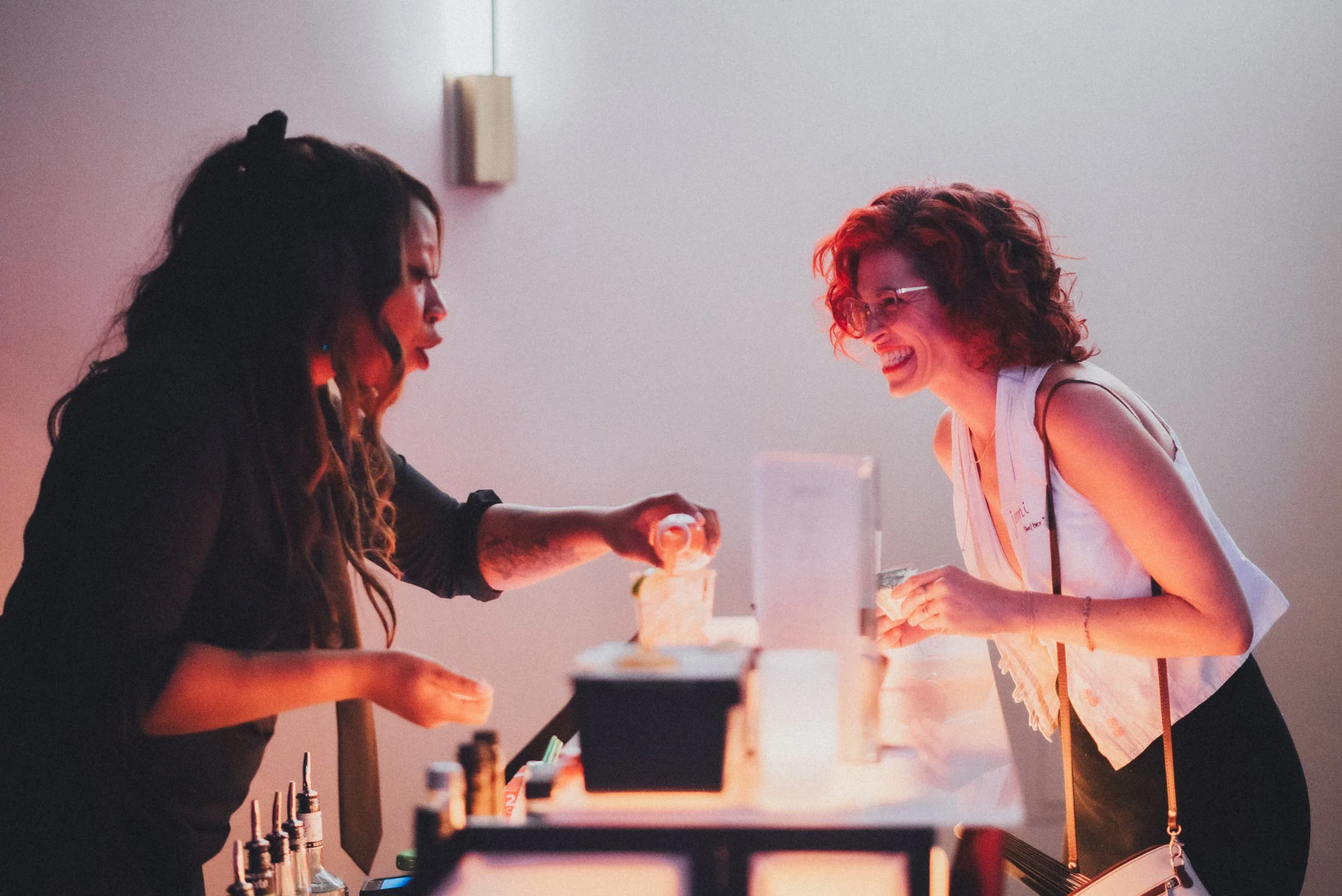 Two women serve customers at a dessert station, smiling and wearing casual clothing, in a brightly lit space.
