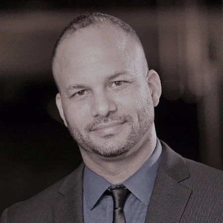 A portrait of a man with short hair, slight beard, wearing a dark suit, blue shirt, and tie, smiling subtly. Matt Winchester. Tessitura.