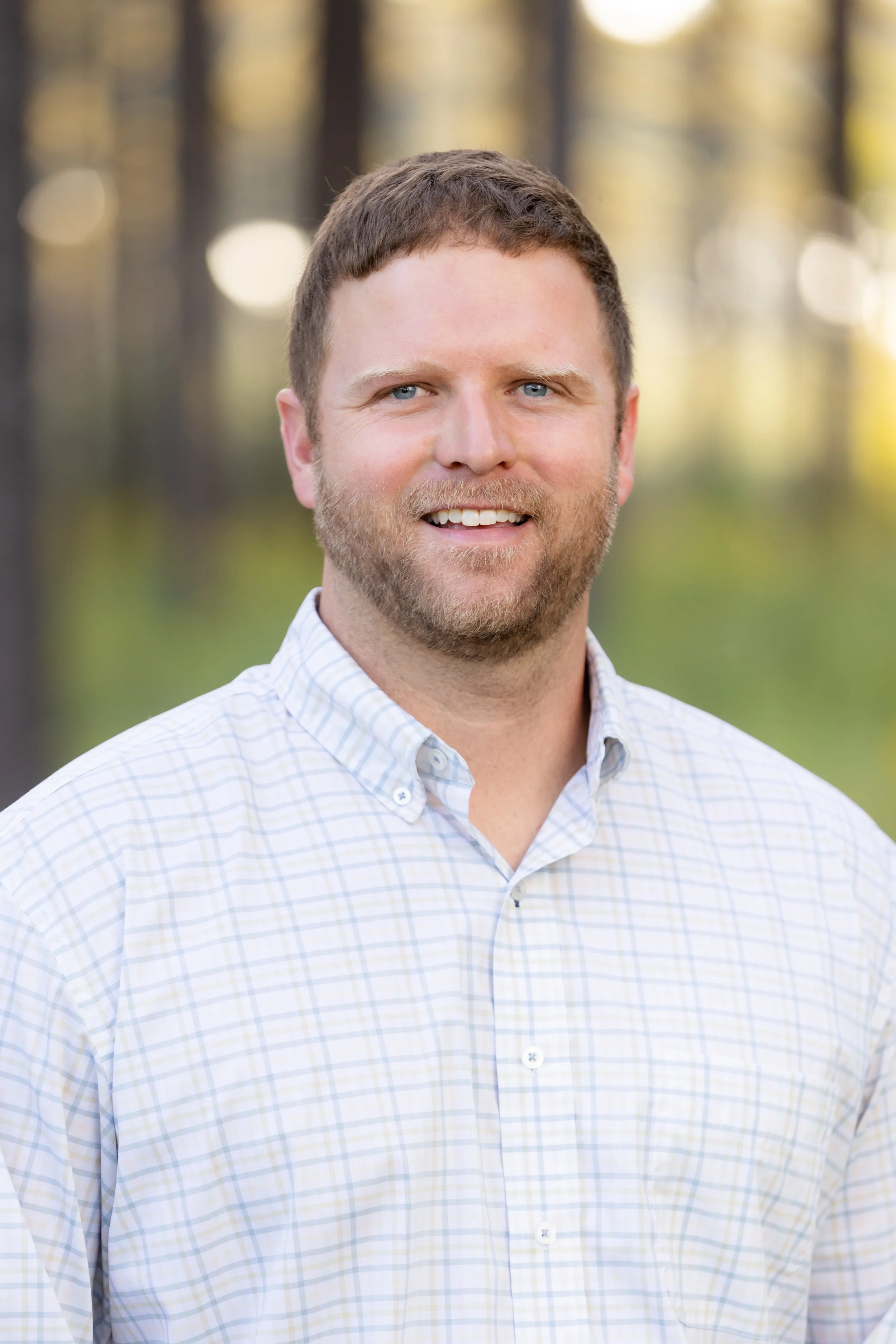Greene Forest & Farm Partner smiling outdoors, wearing a light-colored checked shirt with a blurred forest background.