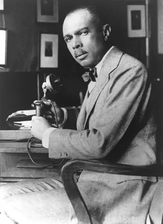 Black and white photo of a man in a suit sitting at a desk, holding a telephone receiver to his ear.