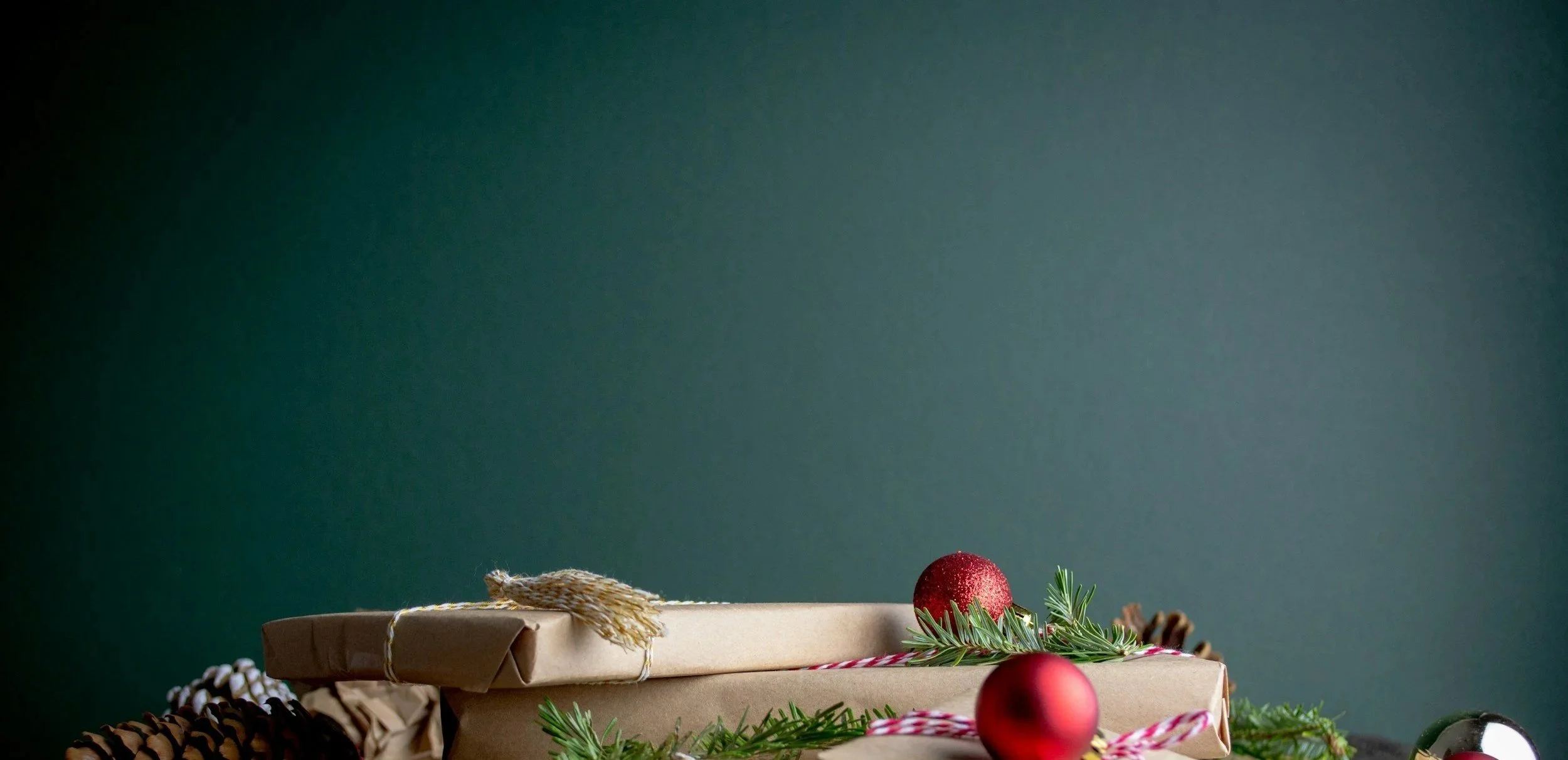 Wrapped Christmas presents decorated with red ornaments, pinecones, green pine branches, and red and white striped ribbon on a dark background.