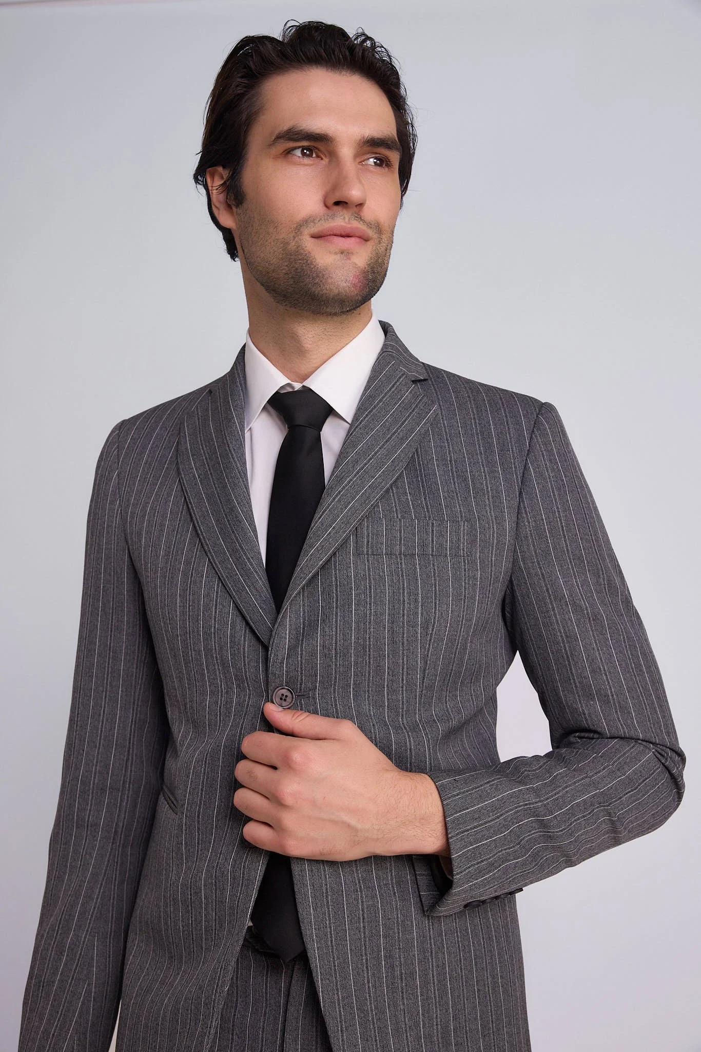 A man dressed in a pinstripe suit, white shirt, and black tie, standing against a plain background.