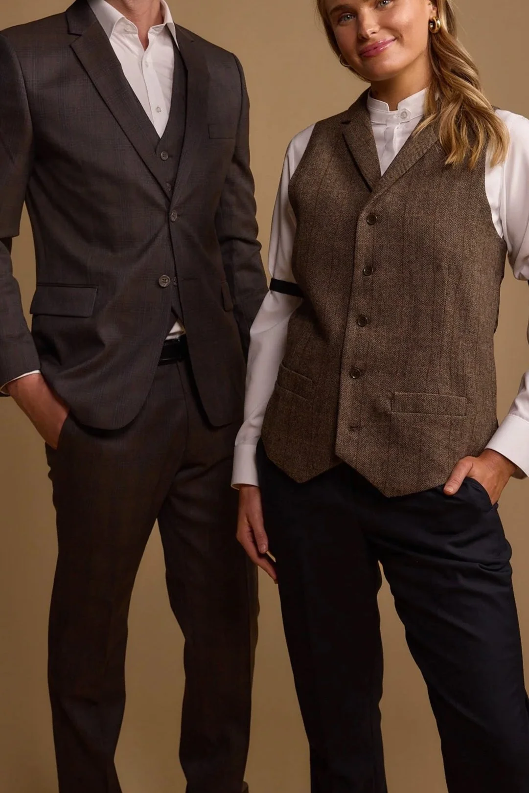 Part of two people dressed in formal business attire, with one person in a dark suit and the other in a vest and shirt with rolled-up sleeves, standing against a plain background.