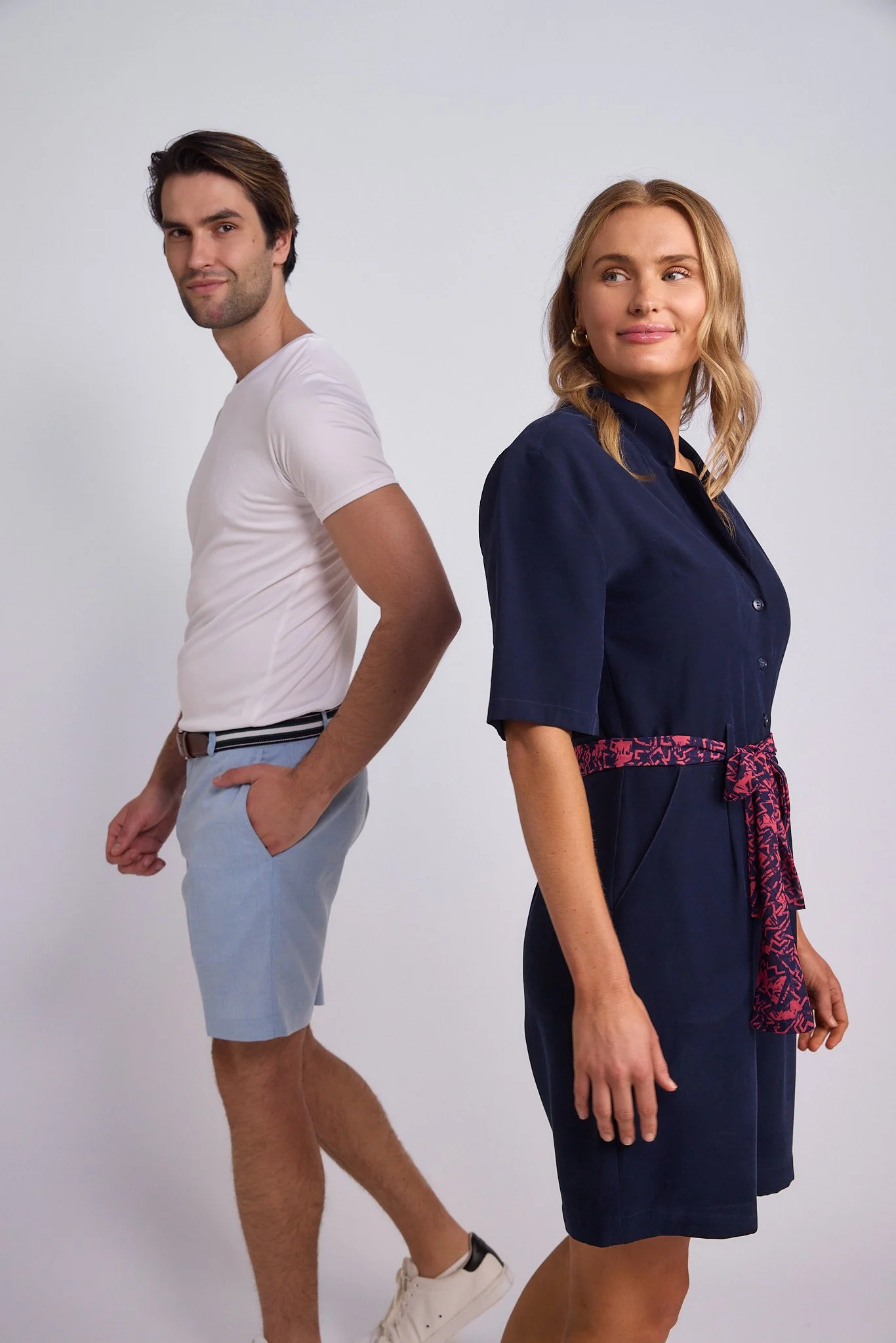 A man and woman stand back-to-back against a plain white background, both looking away from each other.