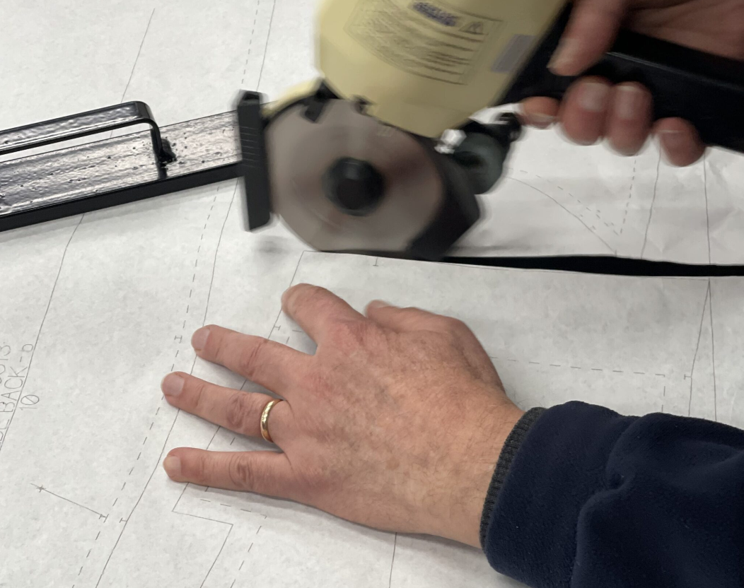 A person using a circular saw to cut a piece of dry wall or sheetrock on a flat surface. The person's left hand is resting on the material, while the right hand operates the saw.