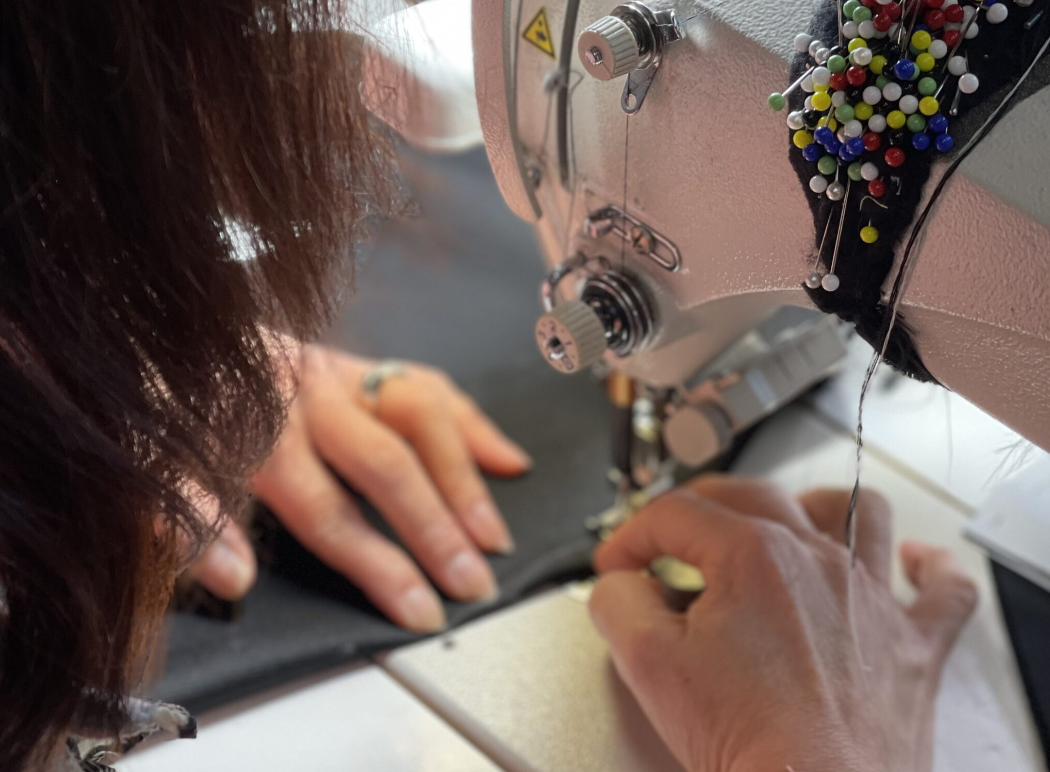 A person sewing fabric using a sewing machine with colorful pins attached to the machine.