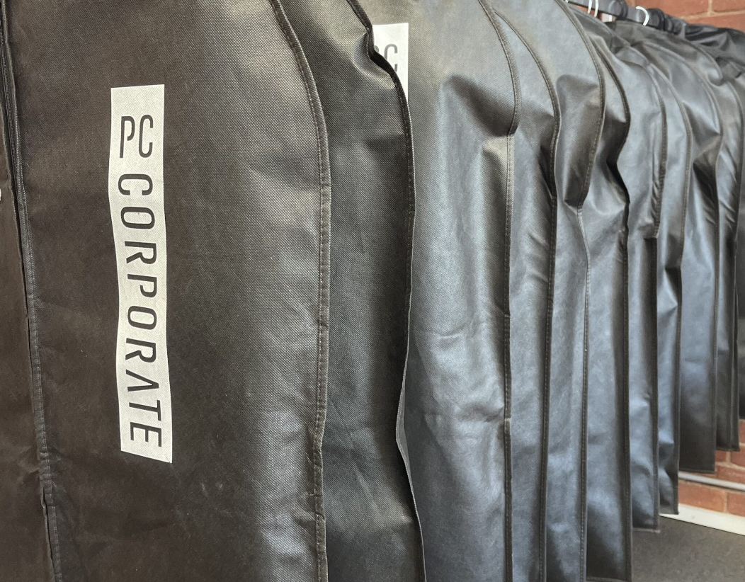 Row of black bags labeled 'PC CORPORATE' hanging on a metal rod.
