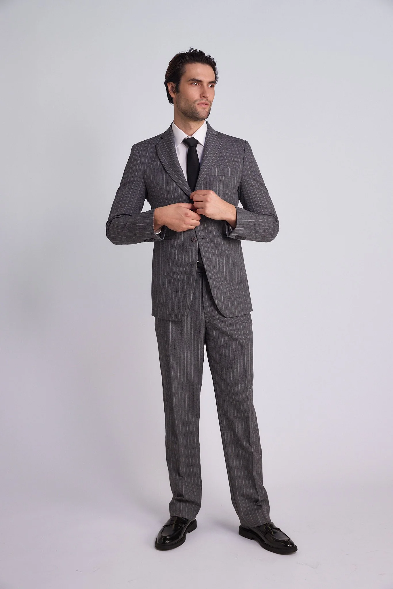 A man in a gray pinstripe suit and black tie posing against a plain light gray background.