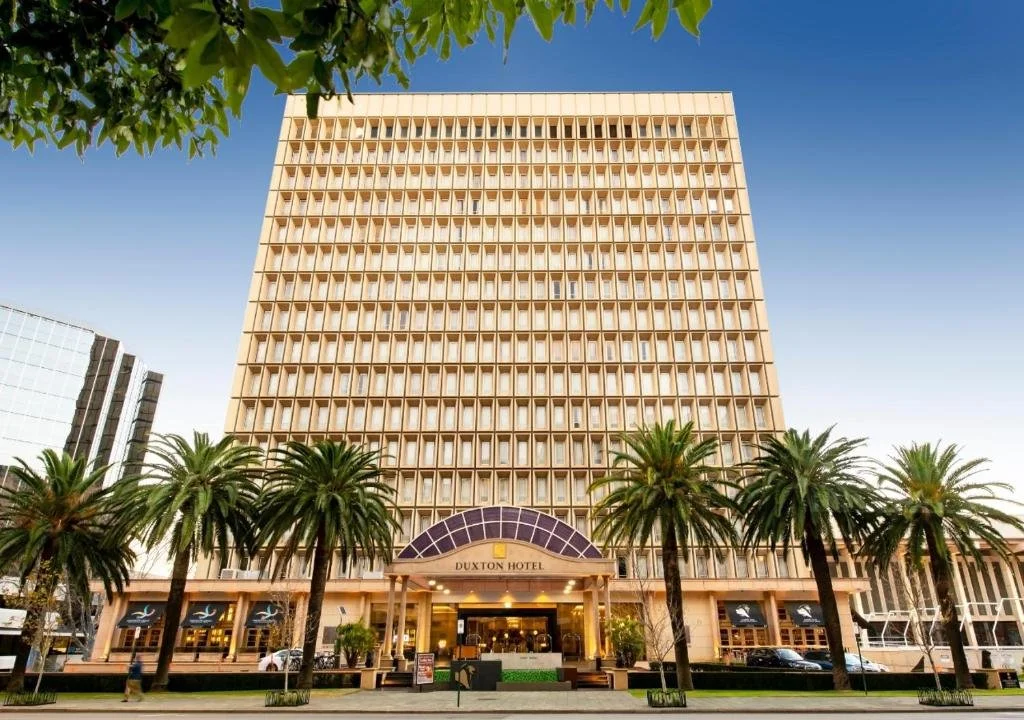 Front view of the Duxton Hotel, a large multi-story building with palm trees in front and blue sky above.