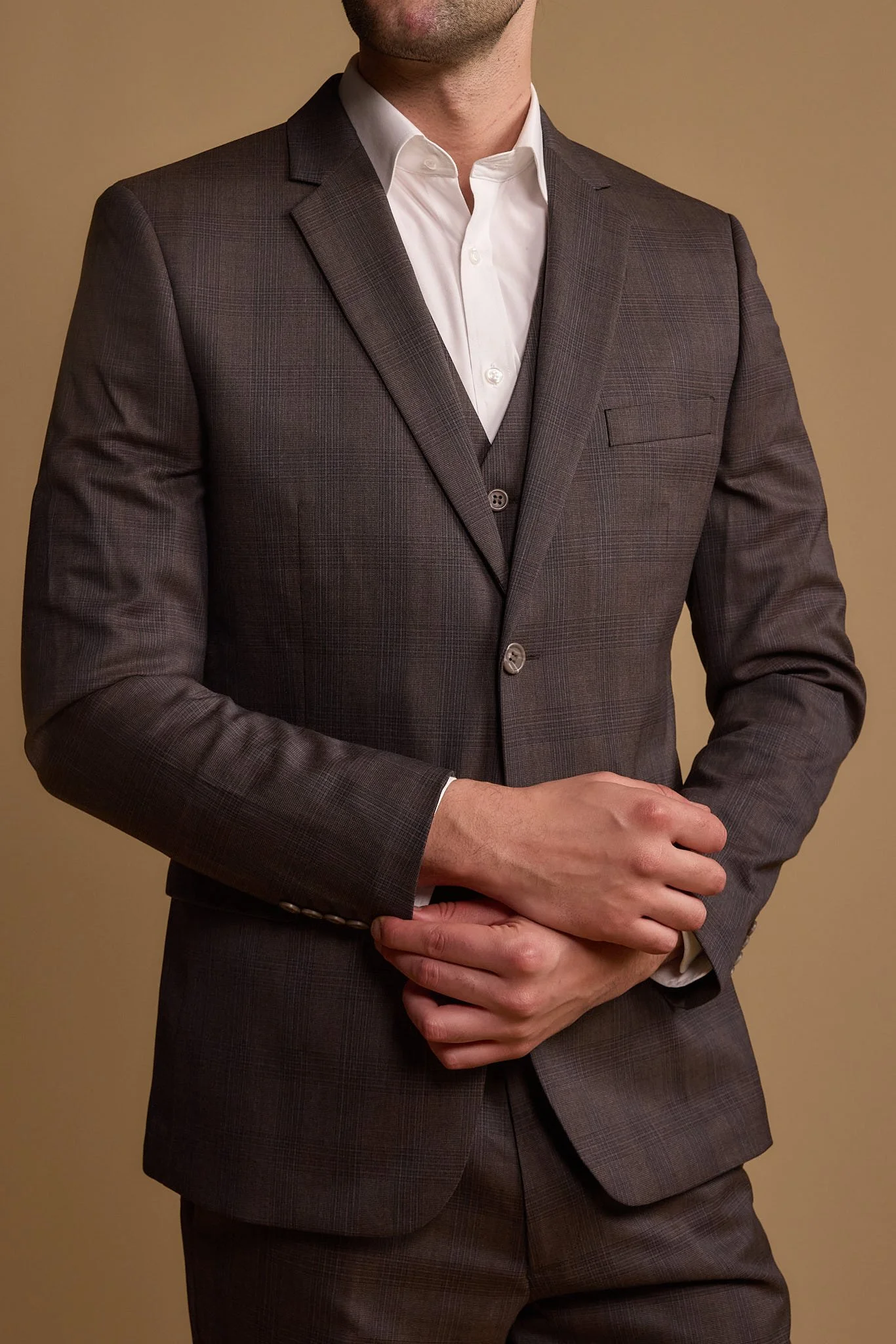 A man dressed in a gray suit with a white dress shirt, no tie, standing against a neutral background.