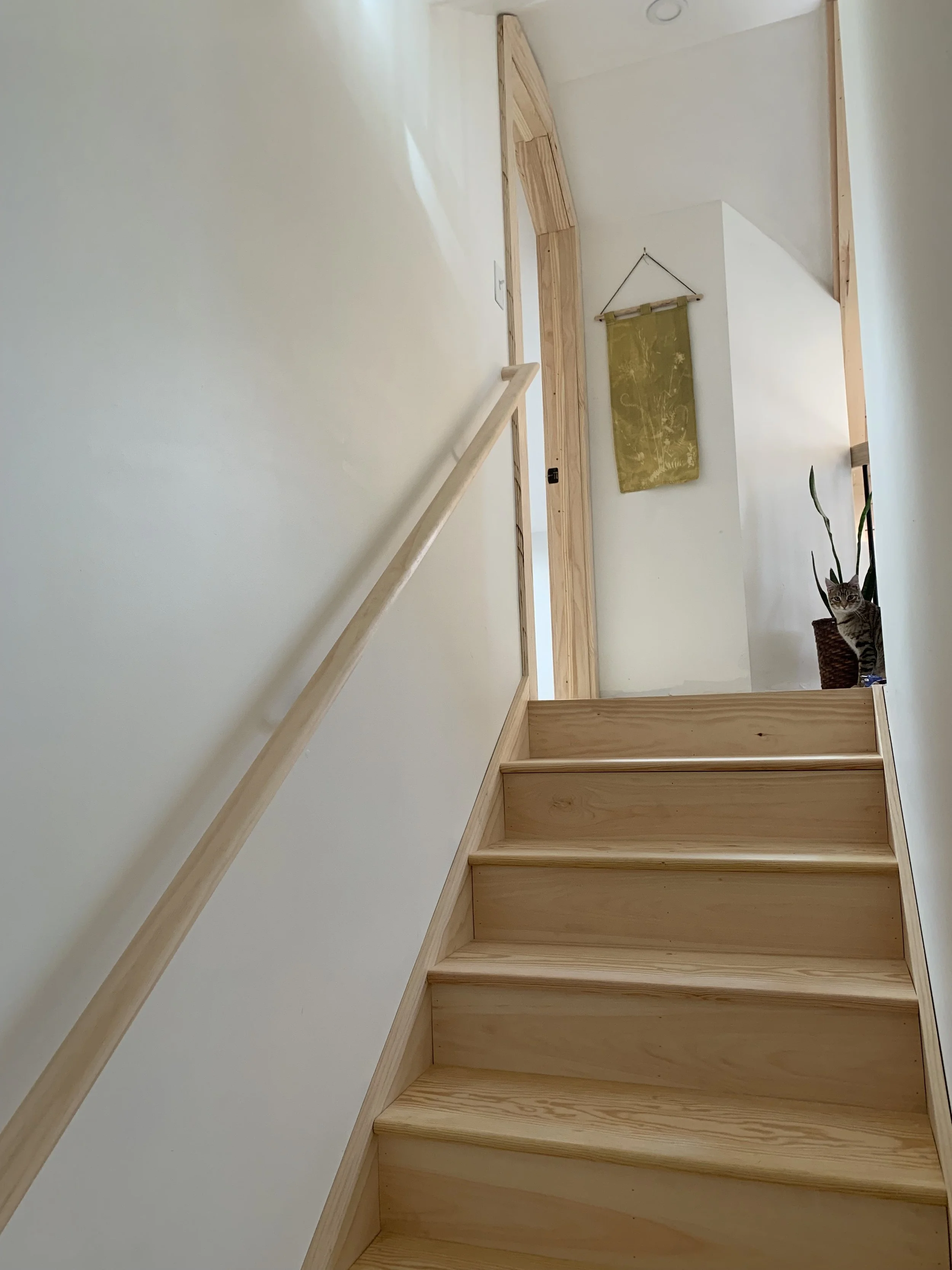 Wooden staircase leading up to a hallway with a potted plant and a small tapestry on the wall.