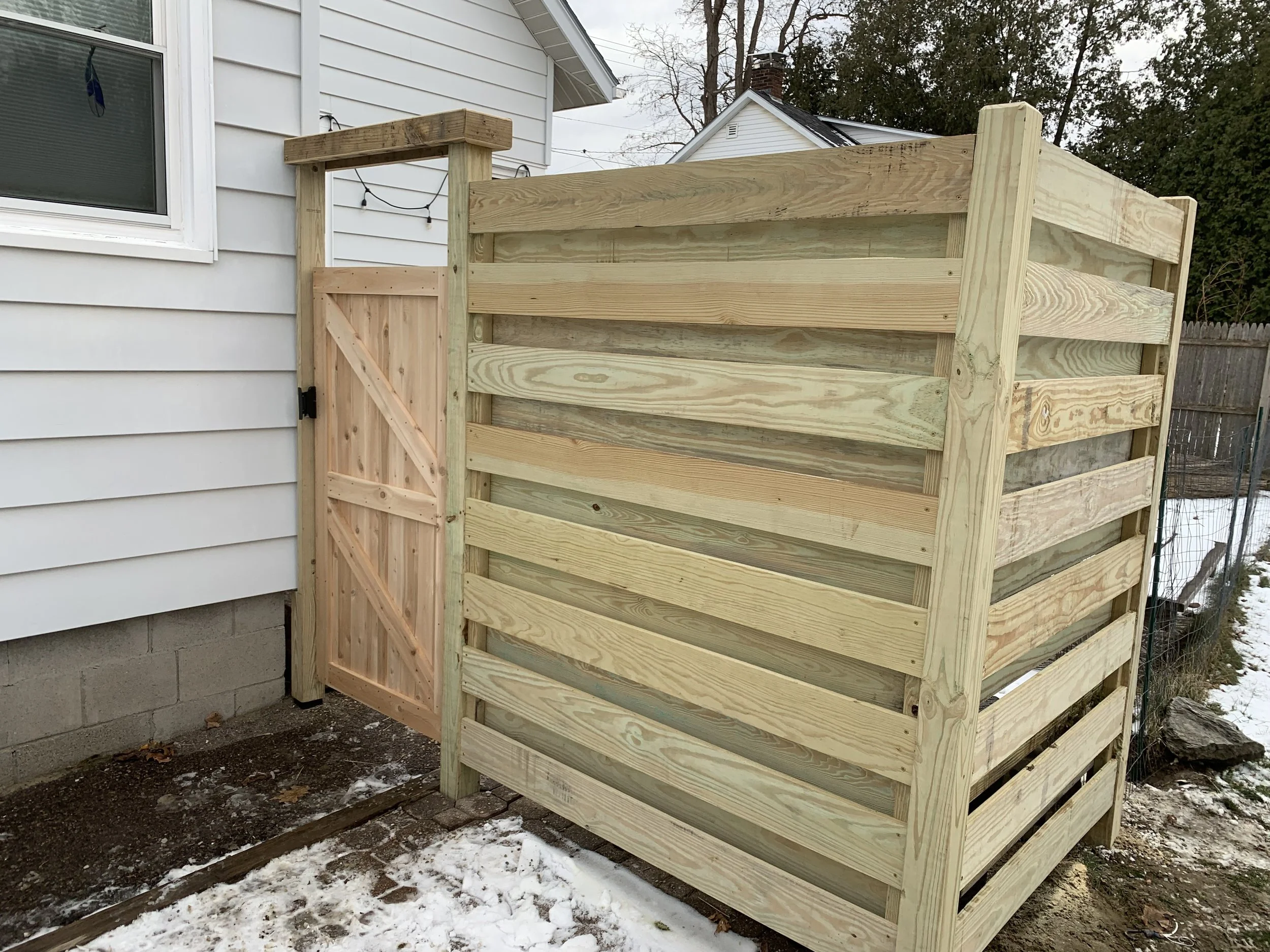 New wooden privacy fence with a gate installed outside a house in winter.