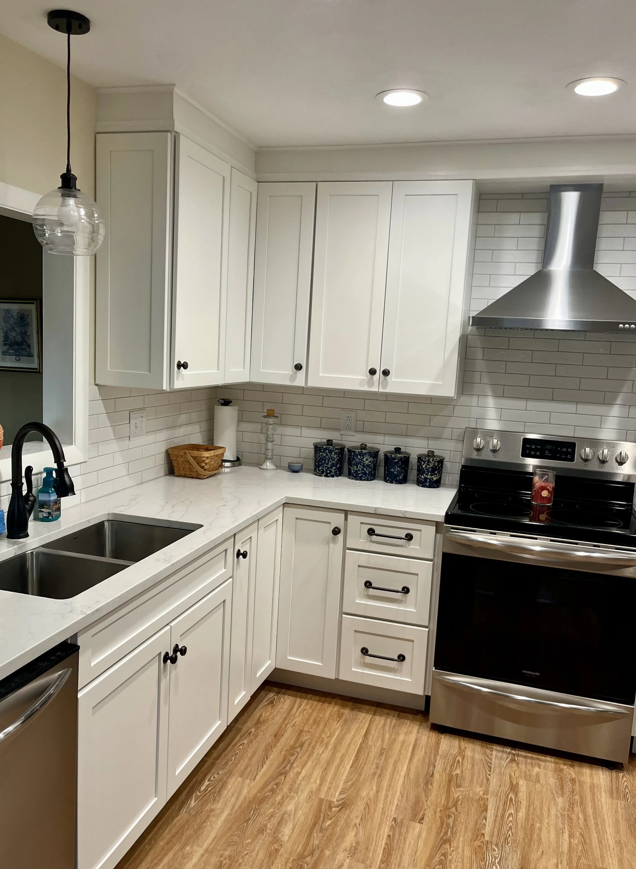Kitchen with white cabinets, marble countertop, stainless steel stove, black faucet, sink, and wood flooring.