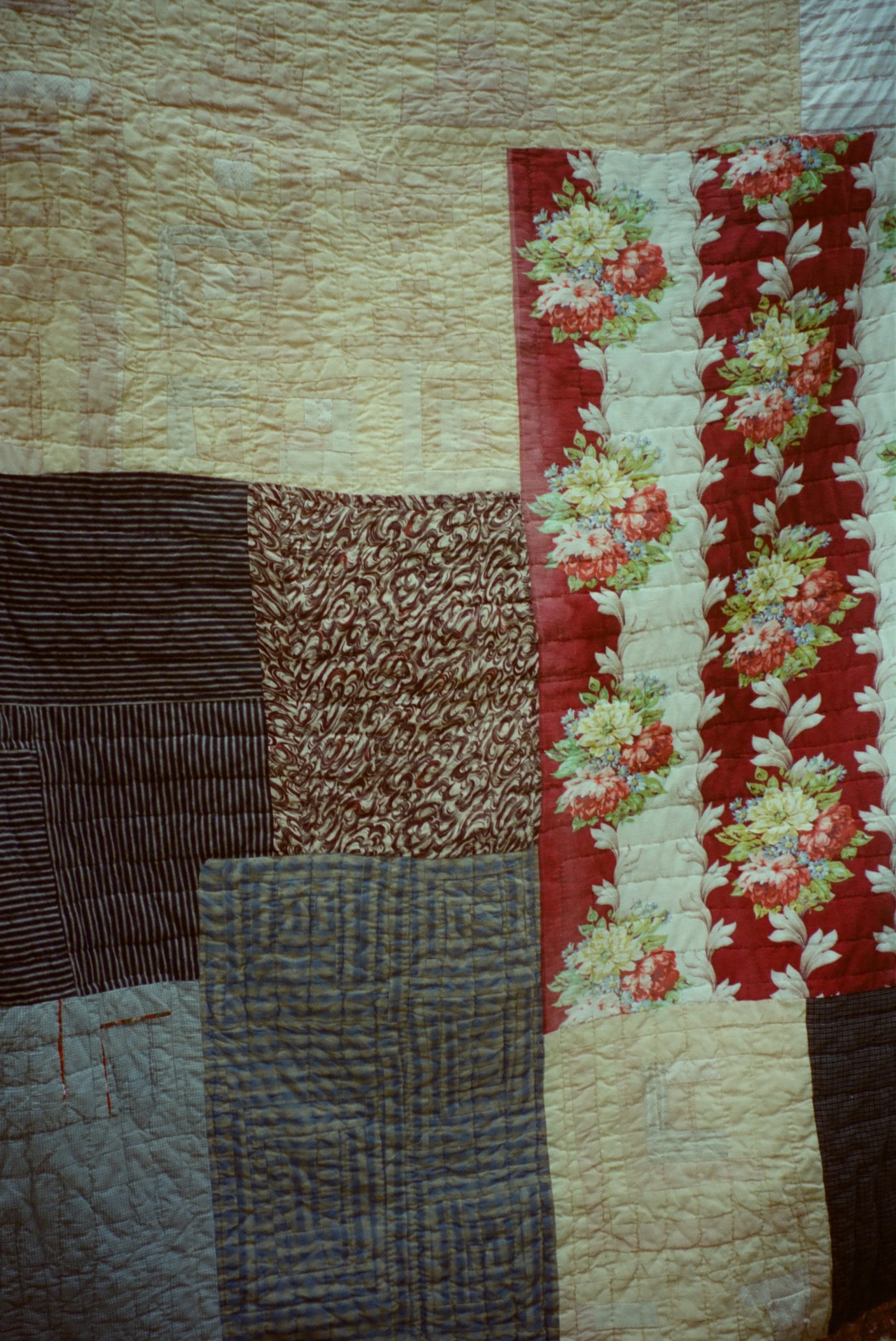 Close-up of a patchwork quilt with various patterned fabric squares, including floral, striped, and plain designs.
