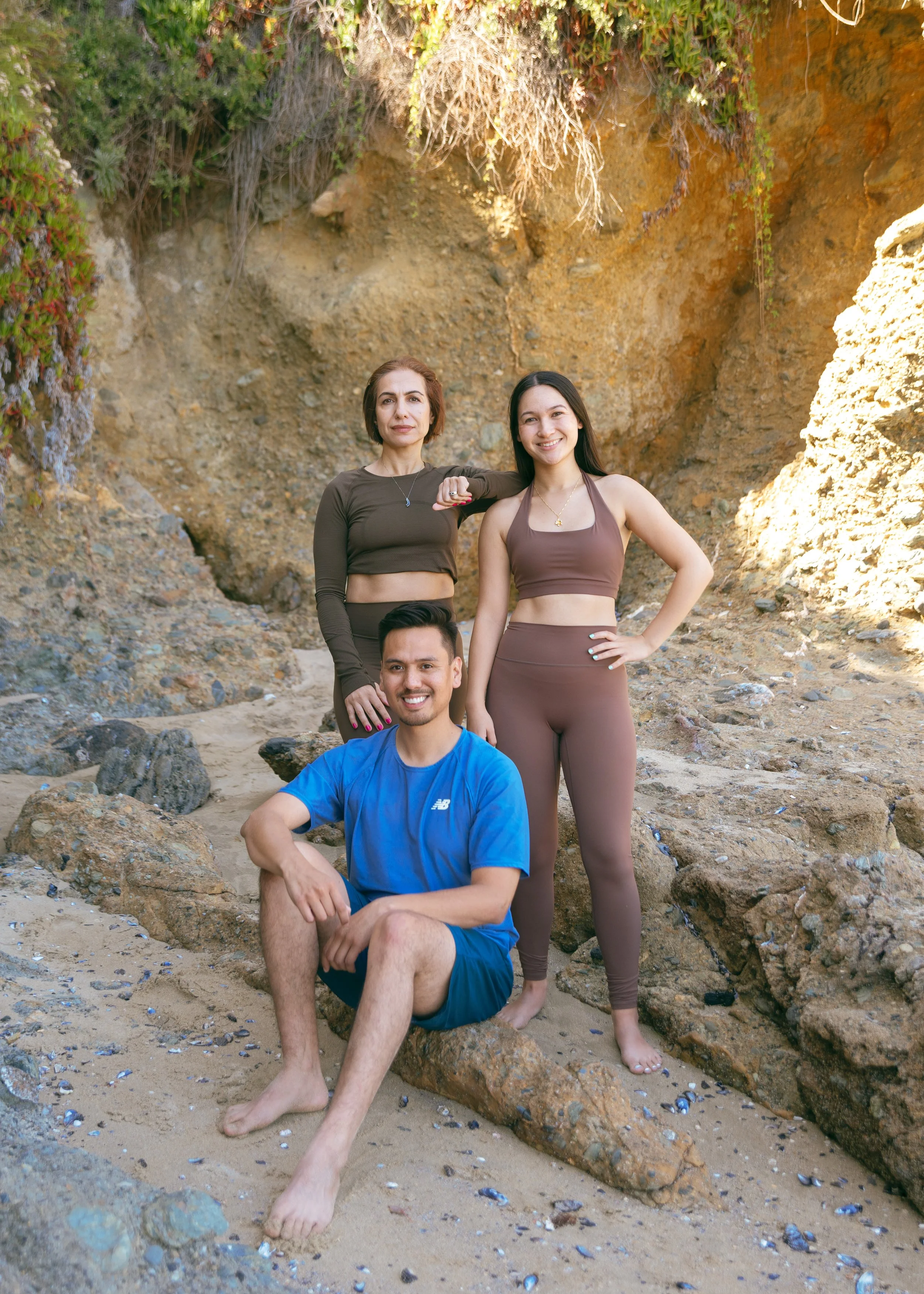 A photo of three people (two women and a male) standing in front of a cliff smiling into the camera.