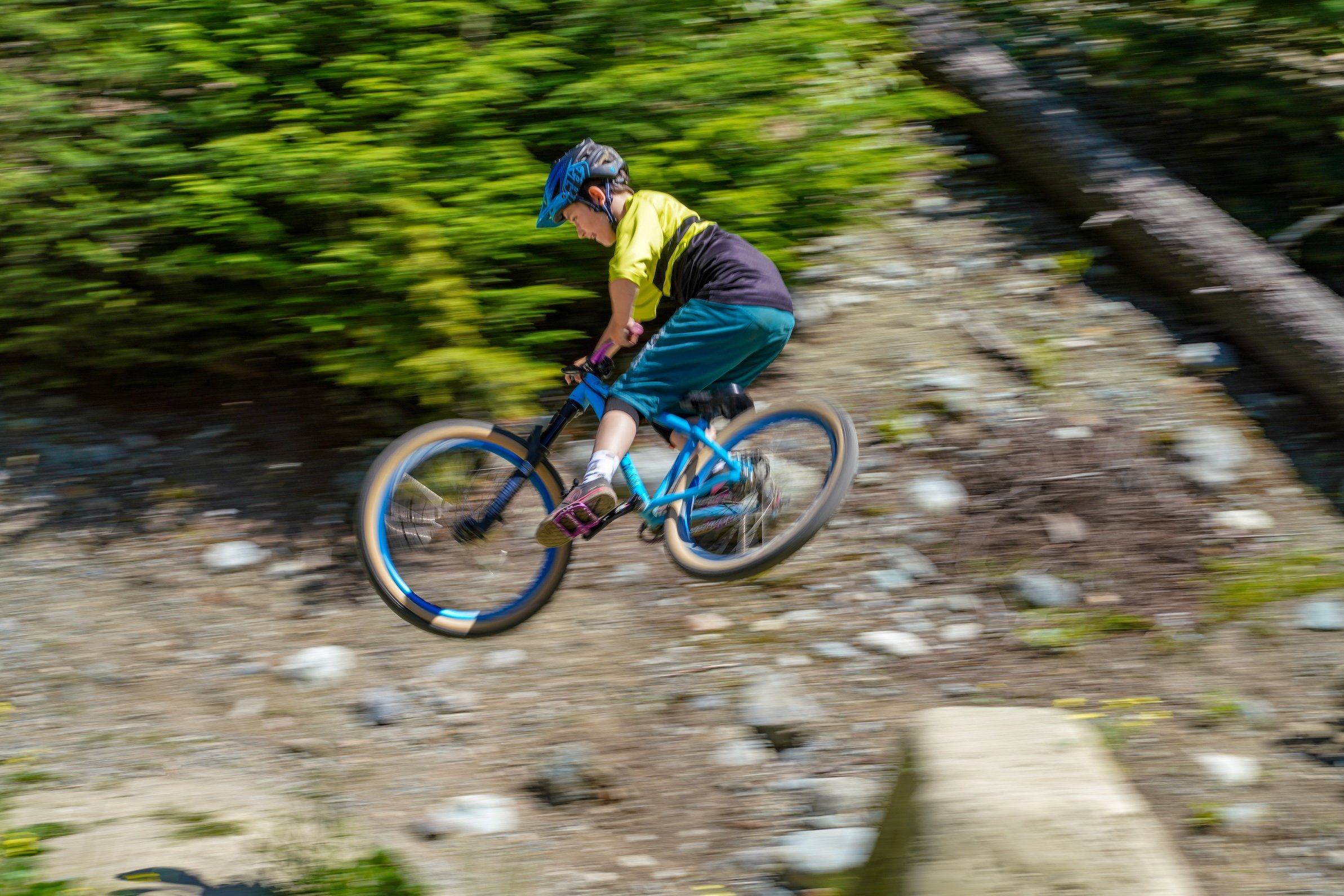 ZEP Racer wearing a blue helmet and yellow shirt is mountain biking at Whistler's famous river dirt jumps.