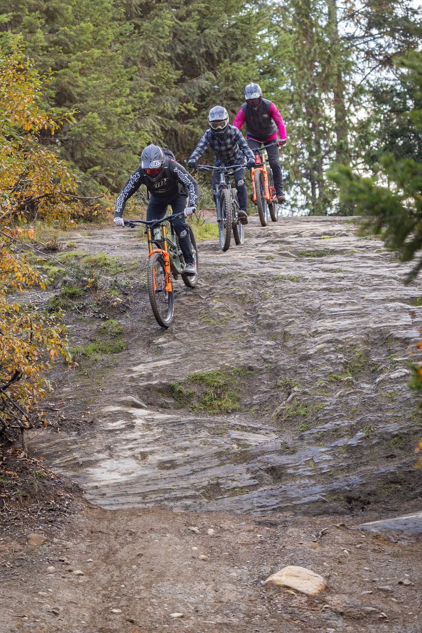 Three mountain bikers descending a rocky trail through the forest.