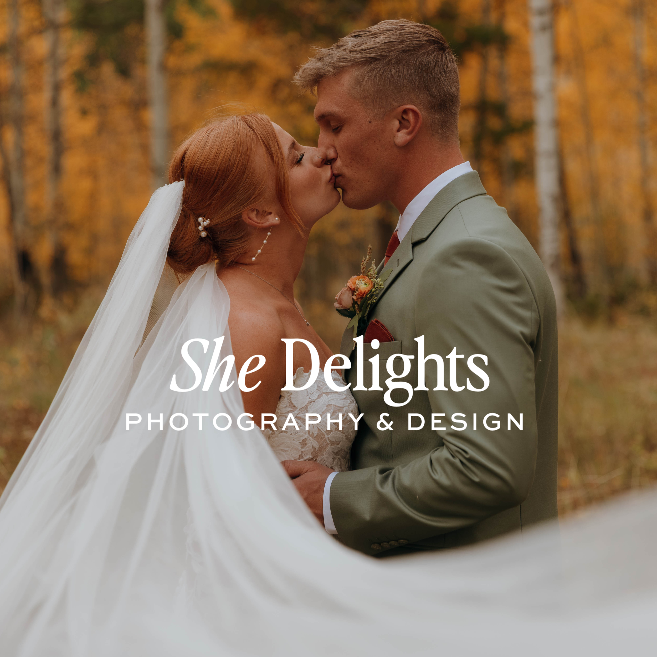 A bride and groom kissing outdoors in an autumn forest, with the bride wearing a white wedding dress and veil, and the groom in a light green suit.