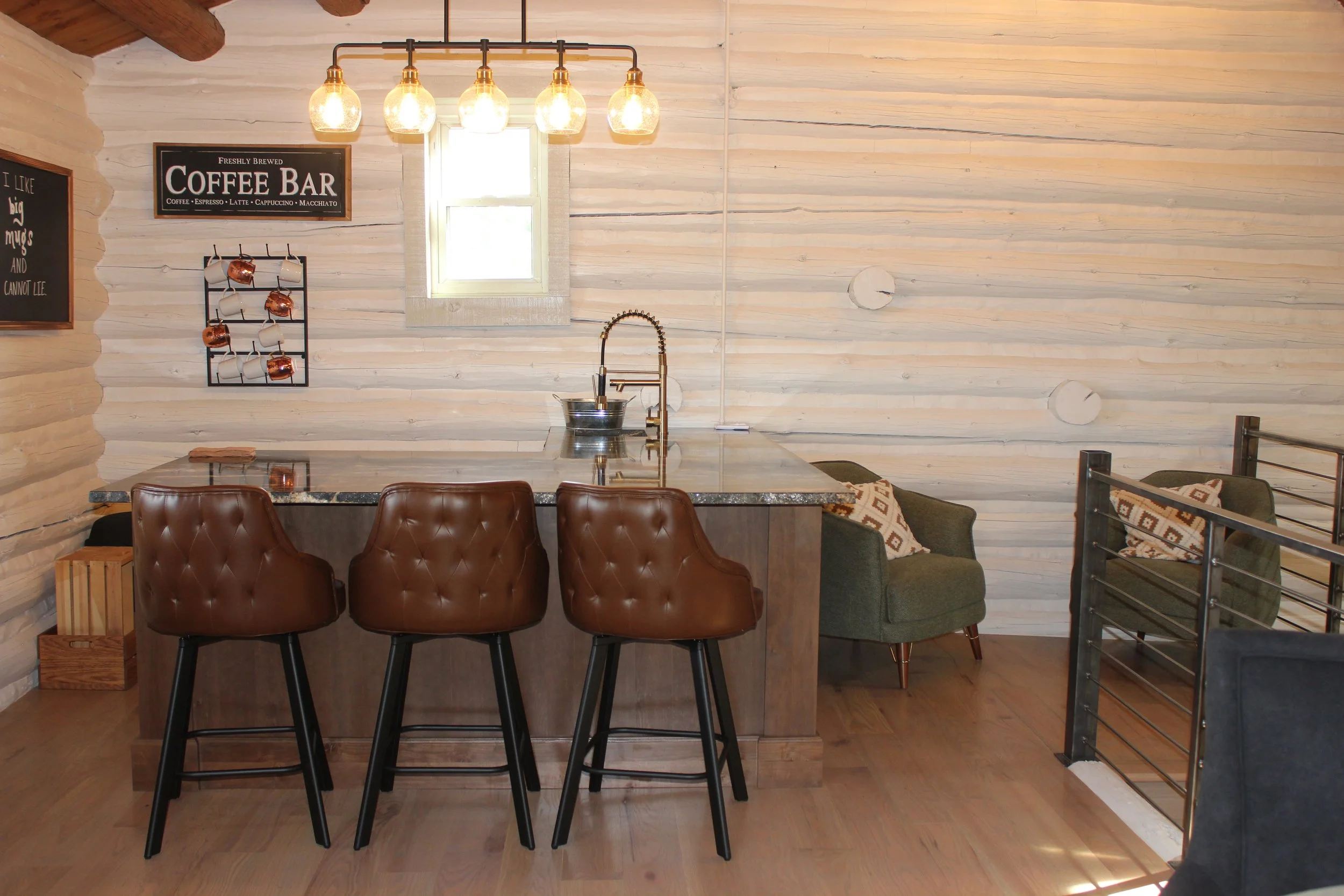 Interior of a cozy coffee bar with a marble countertop, brown leather bar stools, green armchairs with patterned pillows, wooden walls, hanging light bulbs, and a small window.