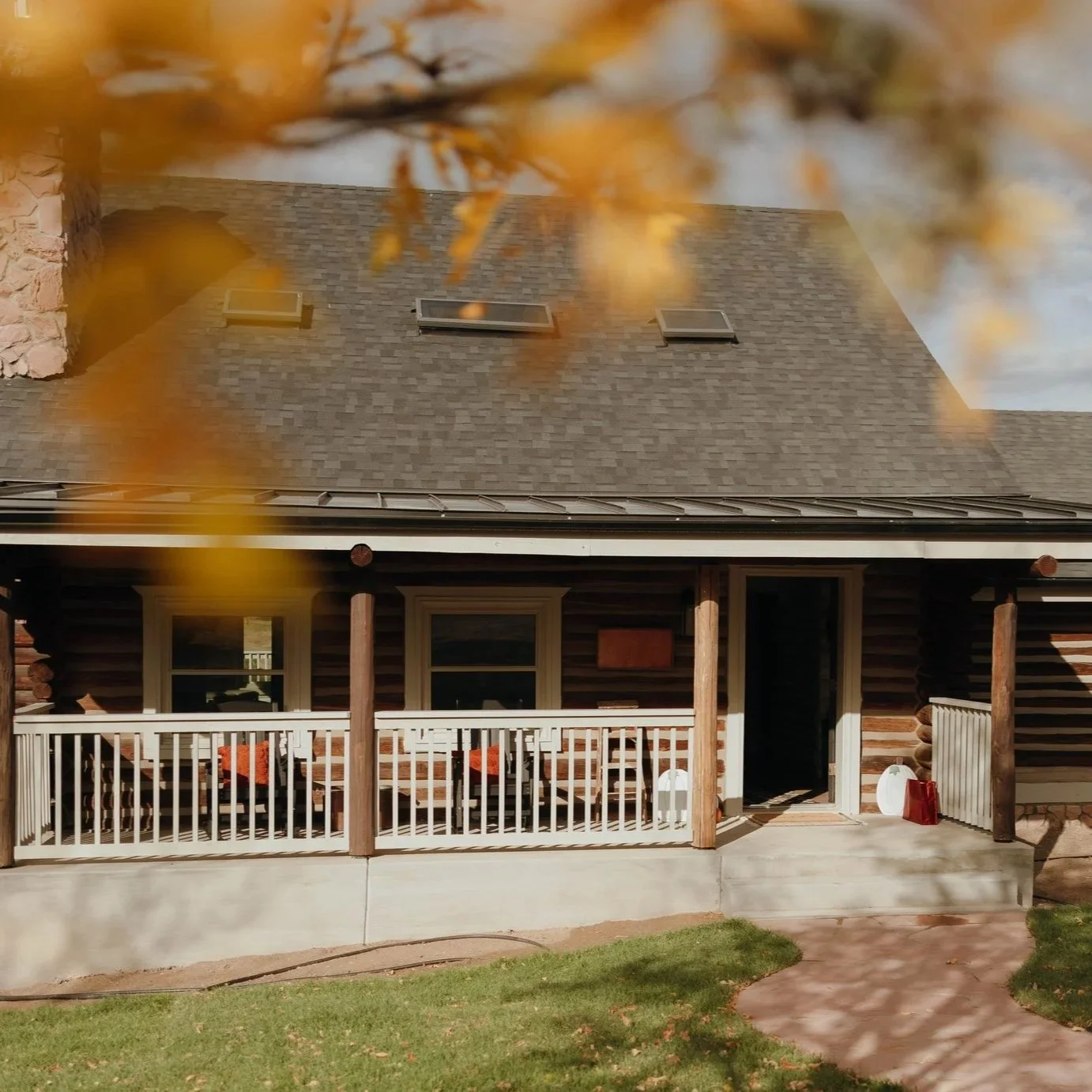 Front view of a house with a porch, two chairs with red cushions, and autumn leaves partially covering the top of the image.