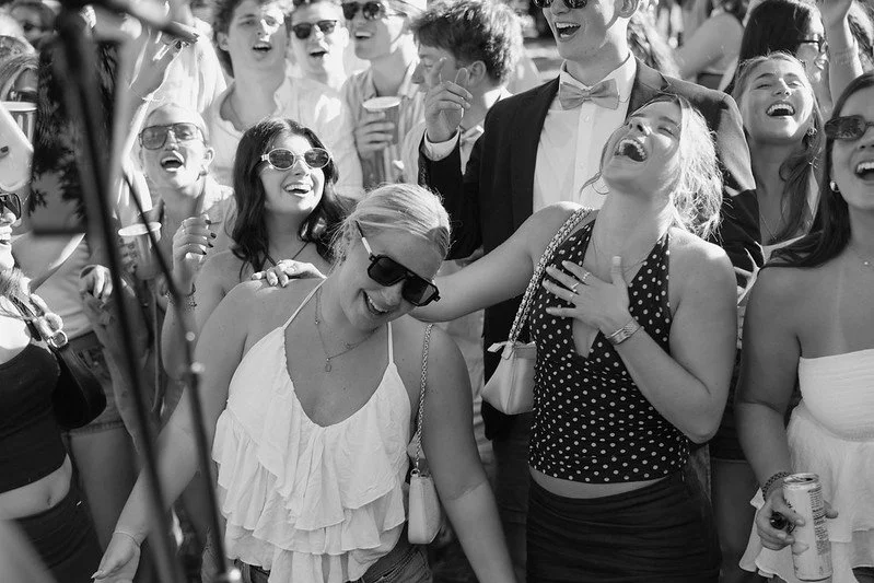 Group of people laughing and enjoying themselves outdoors, some wearing sunglasses and summer clothes.