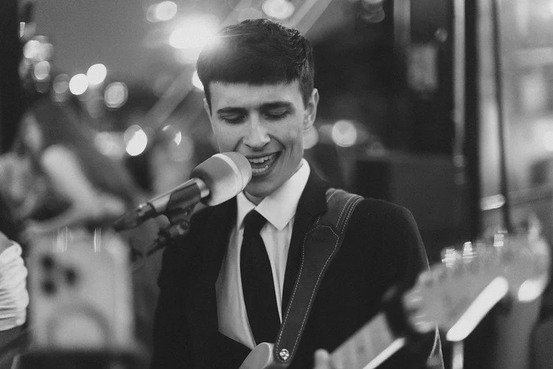 A man singing into a microphone while playing an electric guitar in a dimly lit setting.