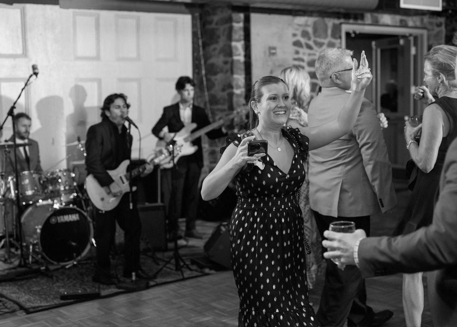 People dancing at a party with a live band playing on stage in background.